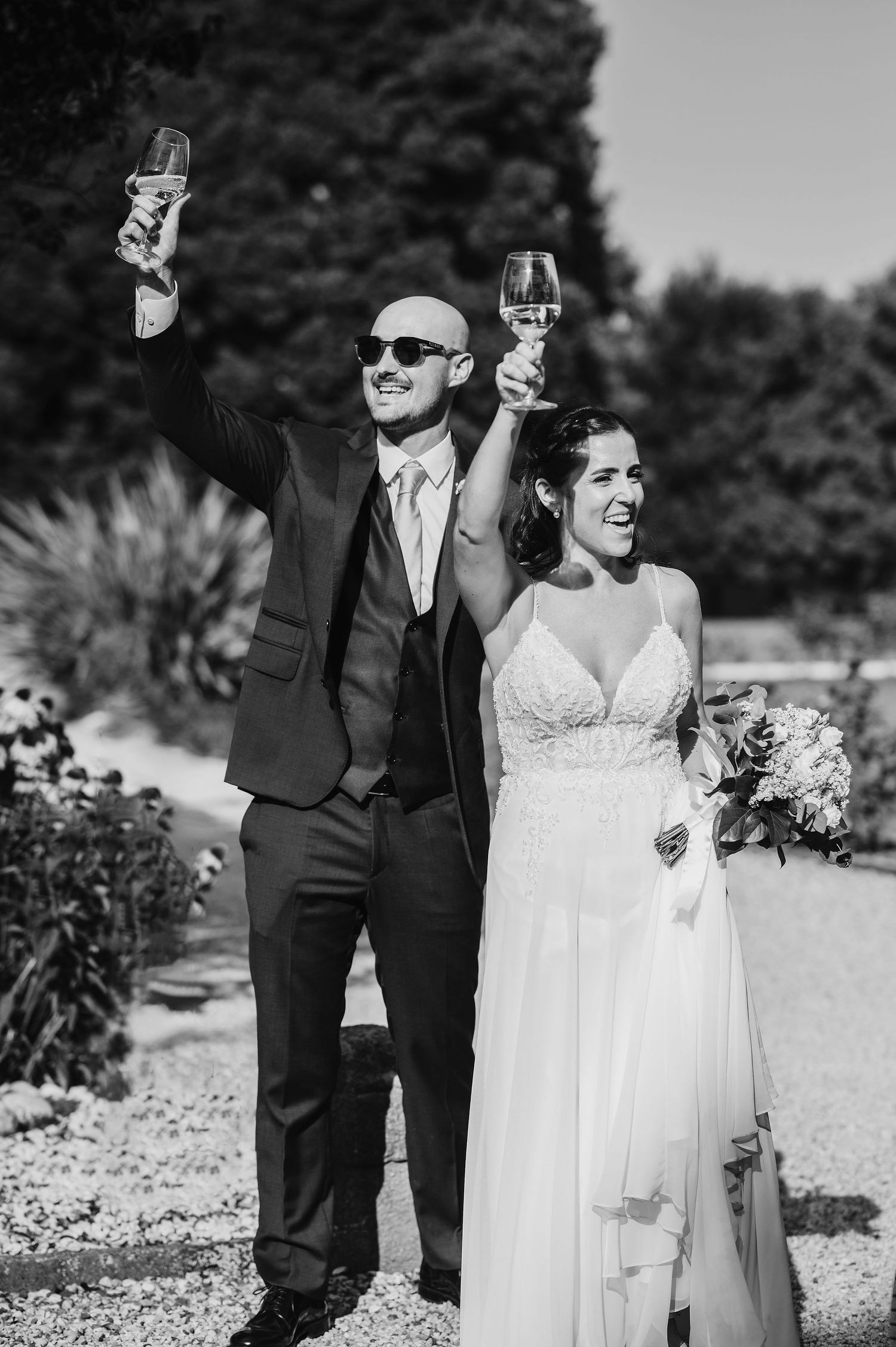 Una coppia di sposi brinda con bicchieri di champagne all'aperto in una giornata di sole.