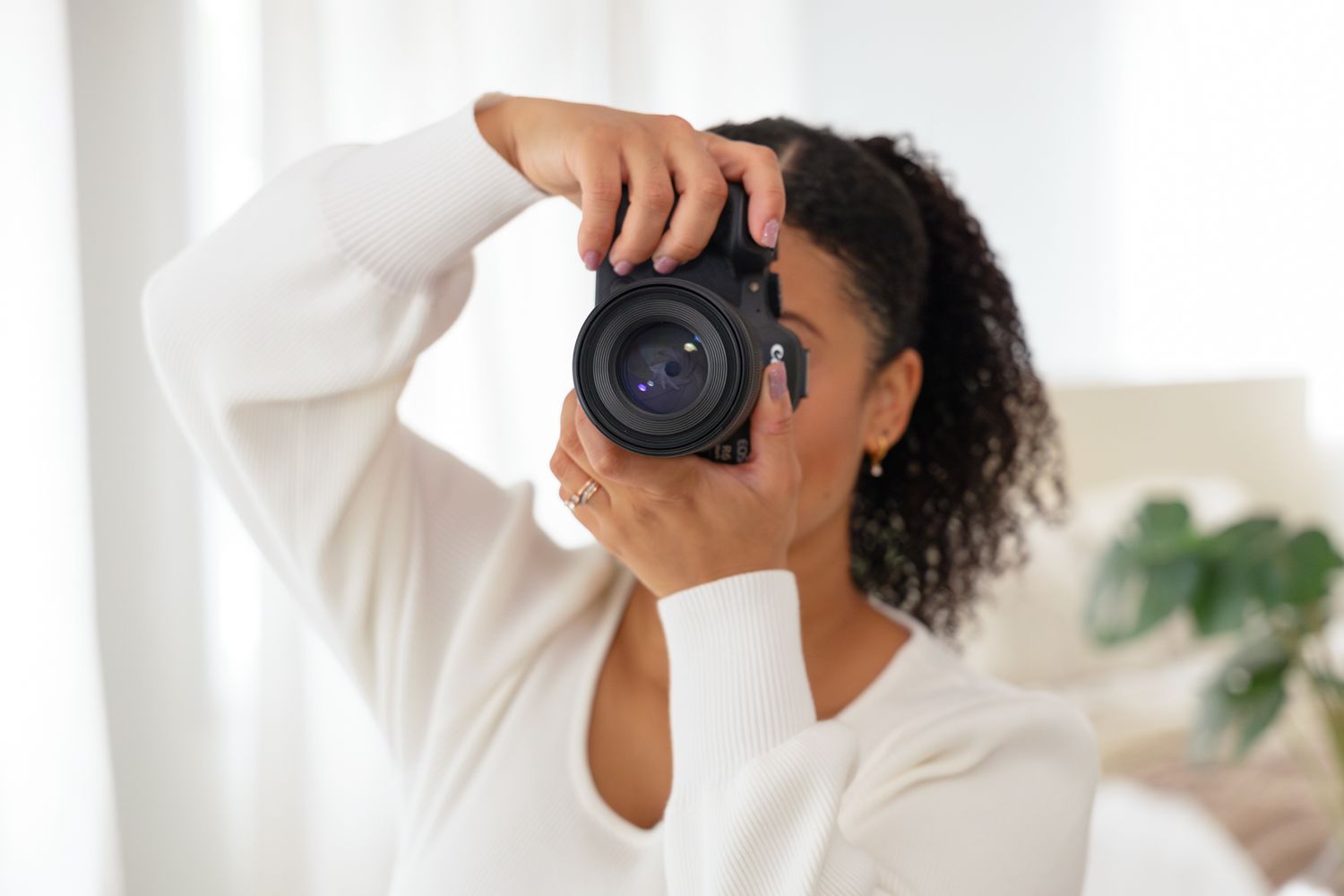 Person in white shirt taking photos with professional camera against light background.