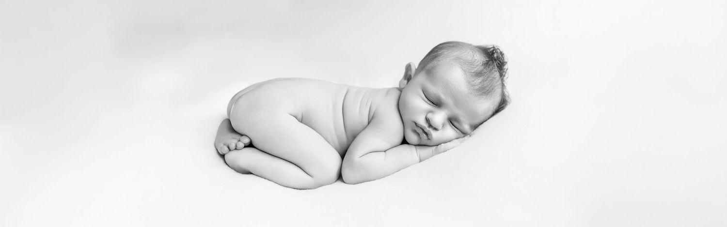 Black and white newborn photography of a sleeping baby curled up peacefully on a white background.