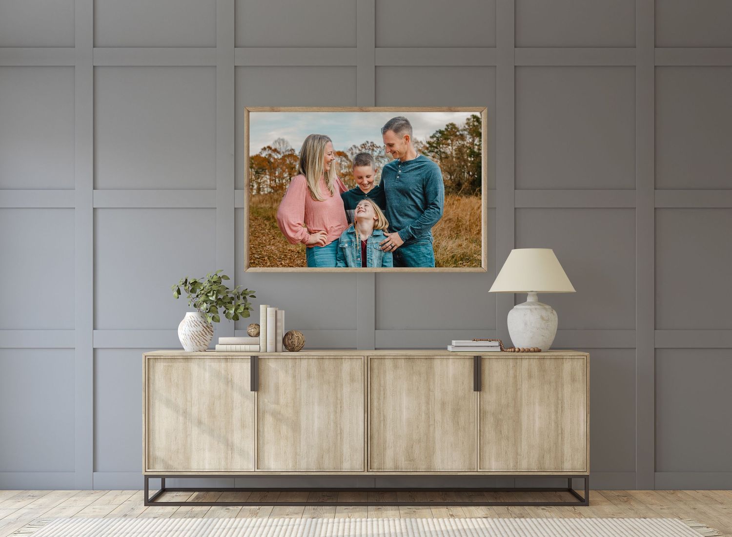 Framed family portrait photo print displayed above a wooden sideboard in a modern gray living room.