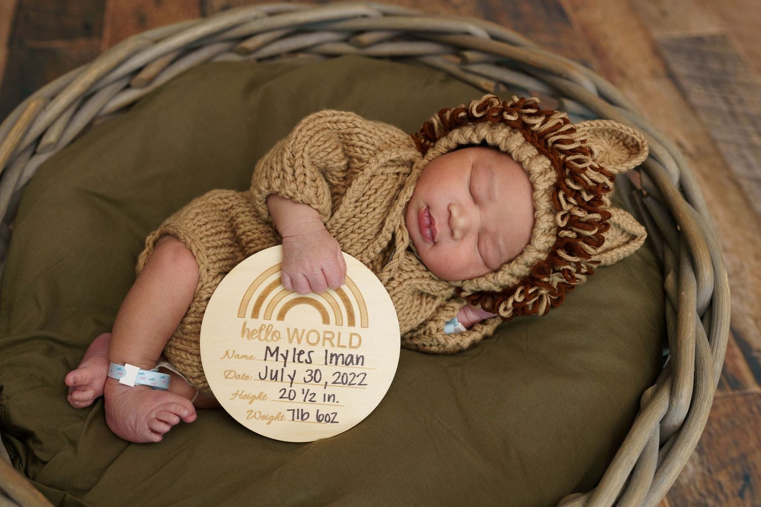 Sleeping newborn in knitted lion outfit with wooden rainbow sign in basket.