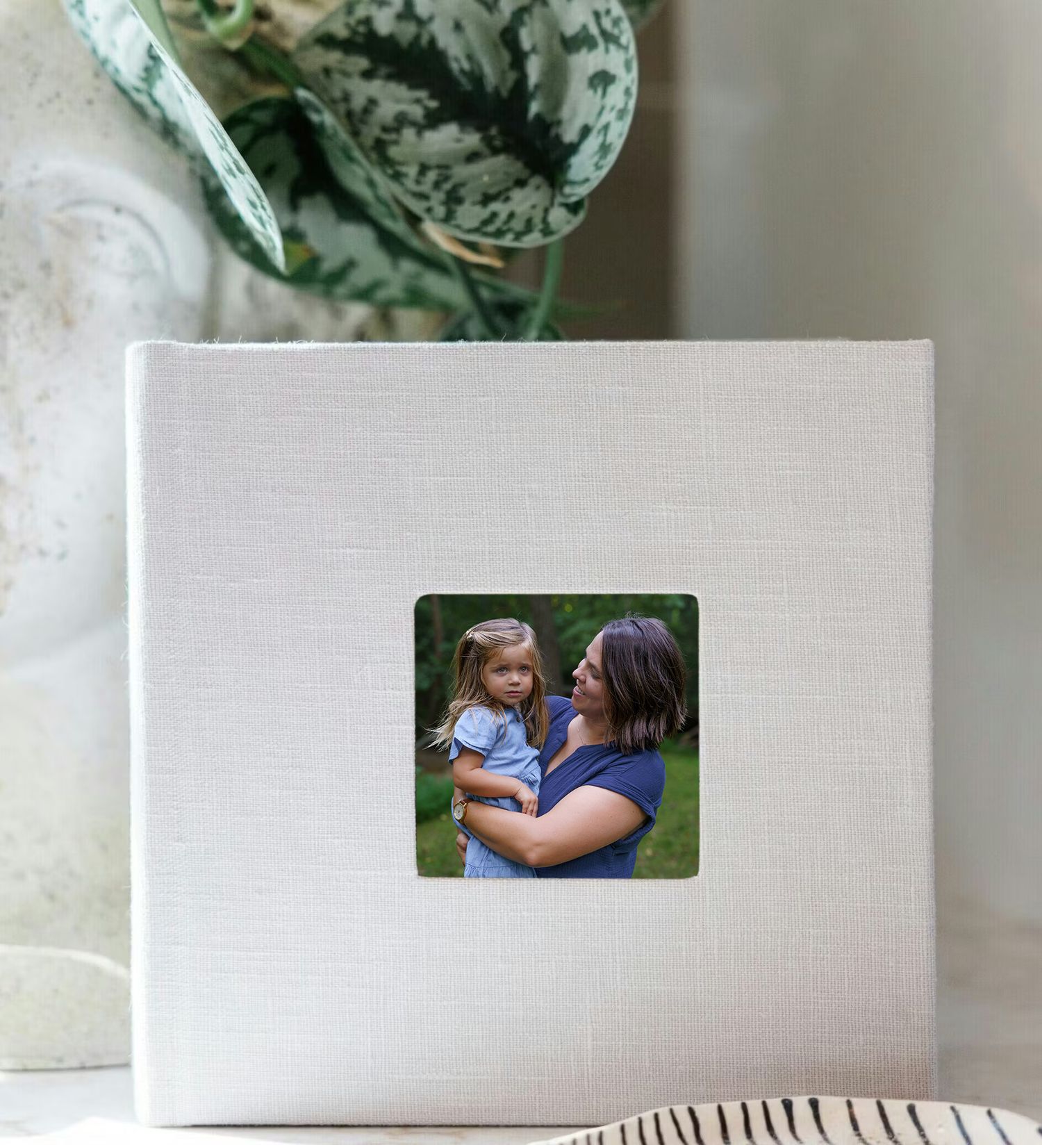 White linen photo album with a small square window featuring a mother holding her young daughter outdoors.