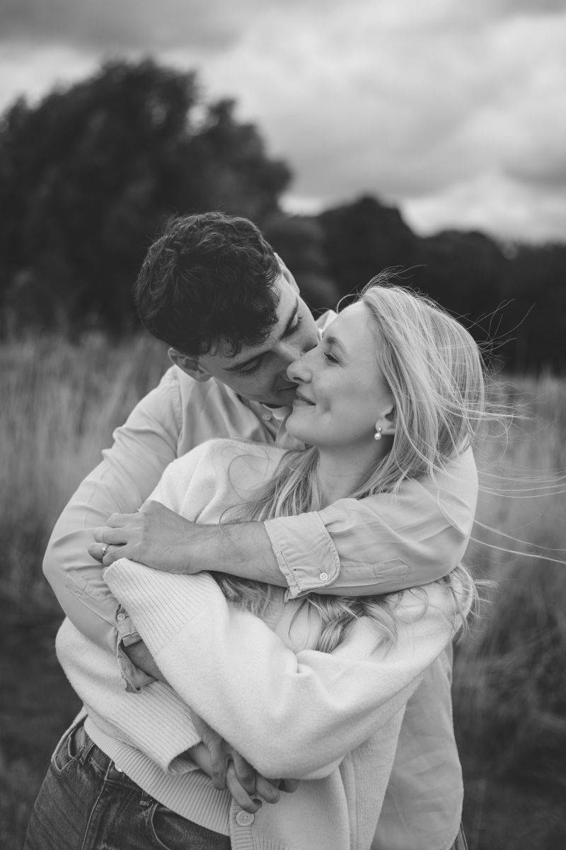 A romantic couple in white clothing embrace and share tender moments in a black and white outdoor photoshoot.