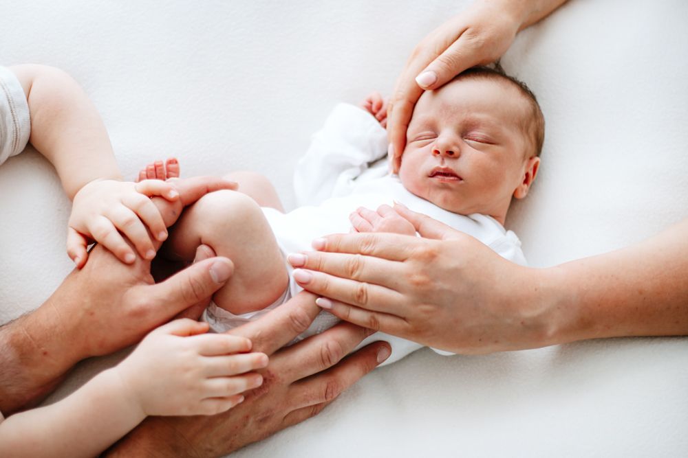 A sleeping infant swaddled in white with hands gently cradling them on a soft white surface.