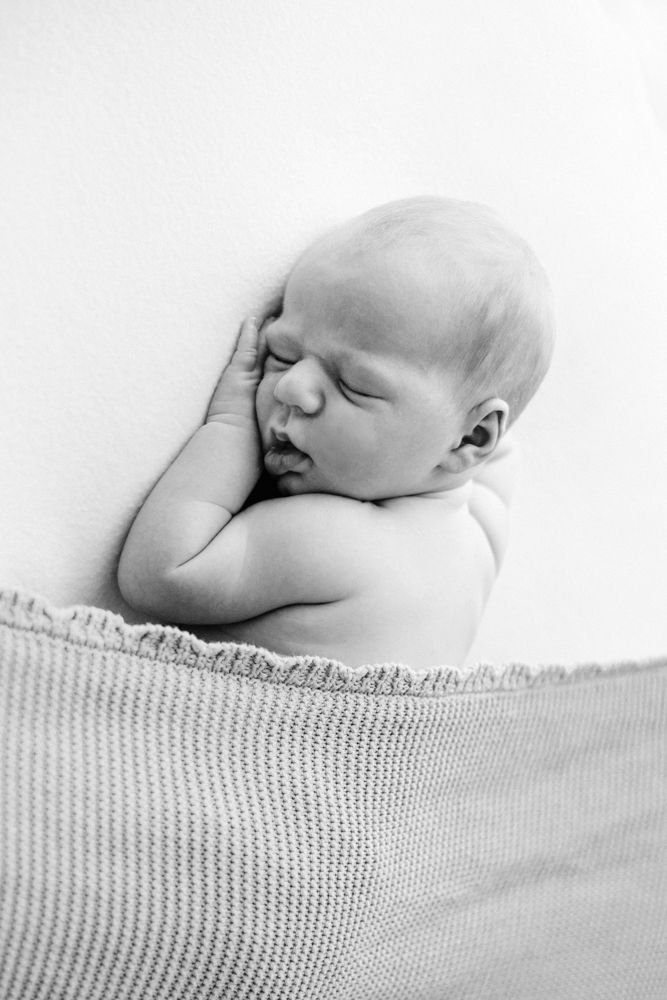 A peaceful black and white portrait of a sleeping newborn baby resting on a knitted blanket.