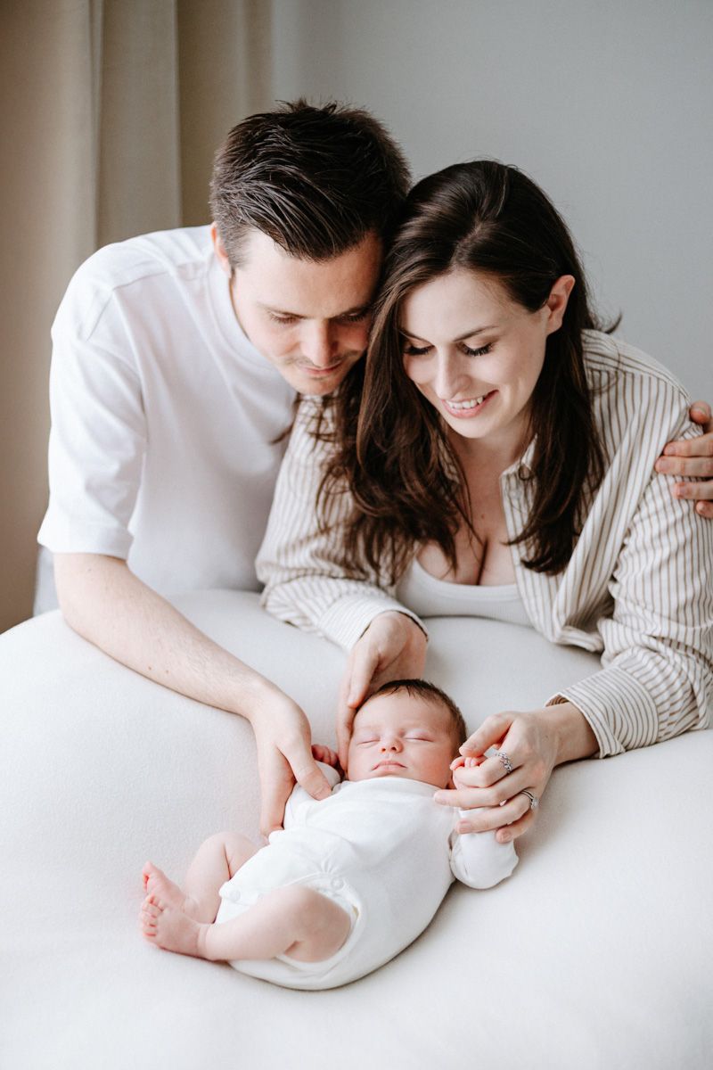 A tender series of photos showing parents lovingly gazing at their sleeping newborn baby on white bedding.