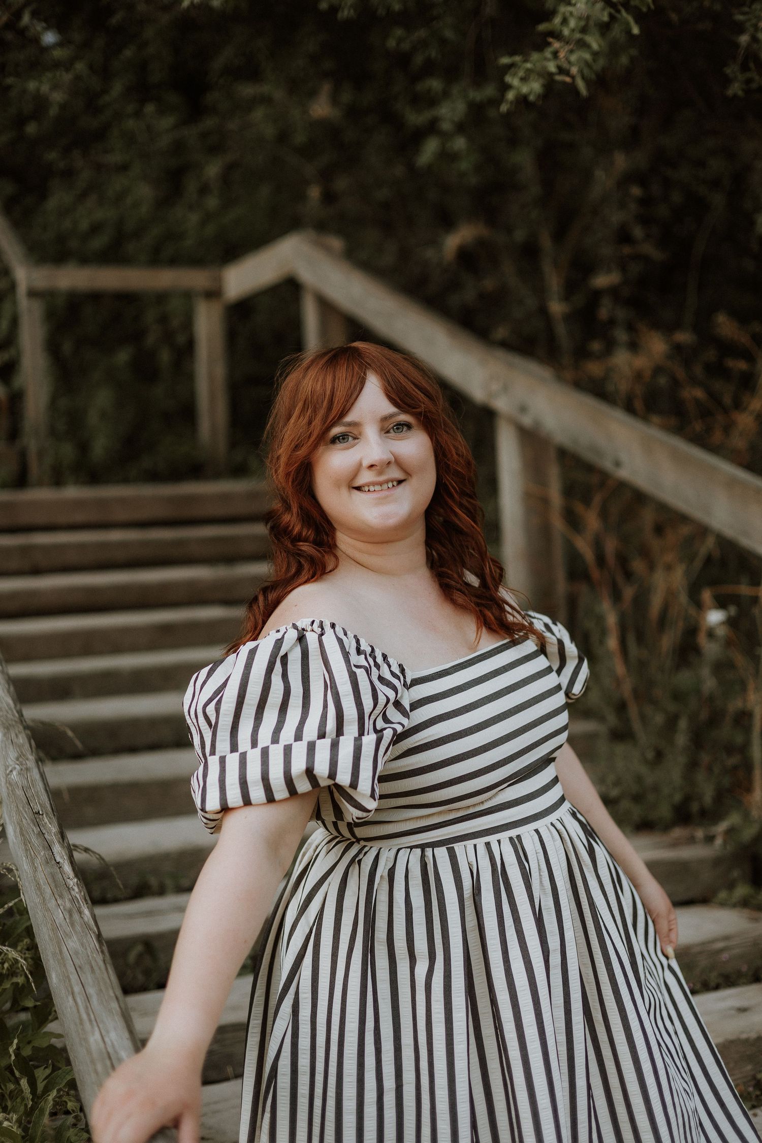 A striped off-shoulder dress is featured outdoors against a natural woodland backdrop.