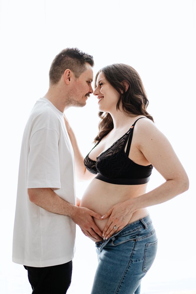 A romantic maternity photo shows an expecting couple sharing an intimate moment in casual attire against a white background.