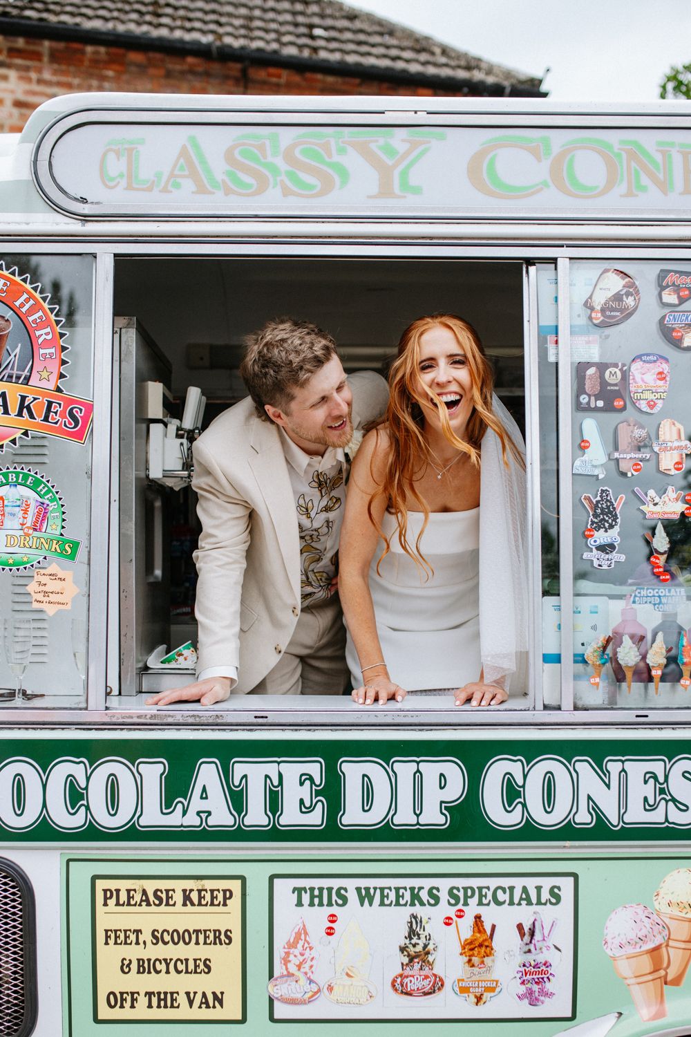 Happy couple leaning out of vintage ice cream truck window with retro signage displaying ice cream flavors and specials.