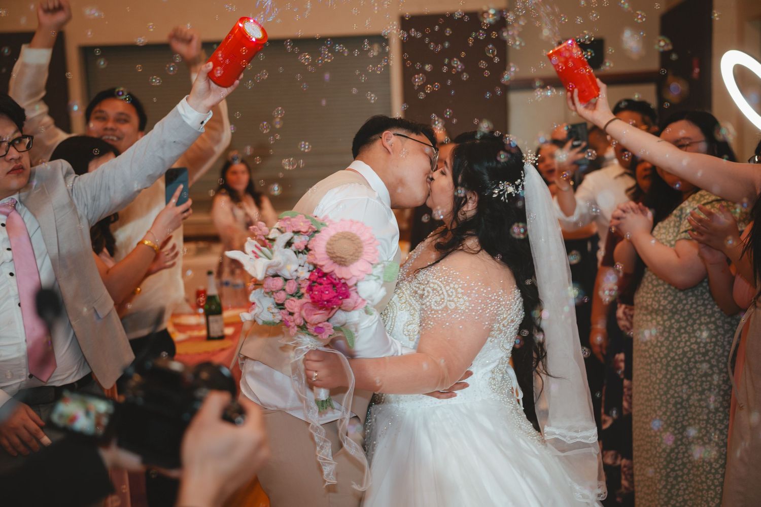 Wedding guests dance and celebrate on a dance floor with red heart balloons and confetti in the air during a reception.
