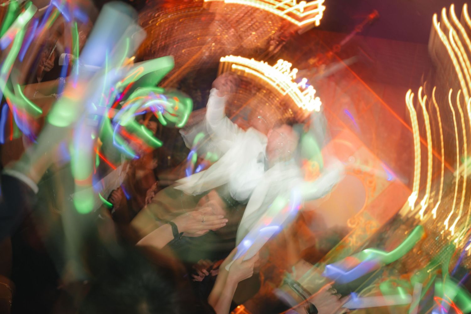 Blurred motion photo of people dancing at a vibrant nightclub with colorful light streaks.