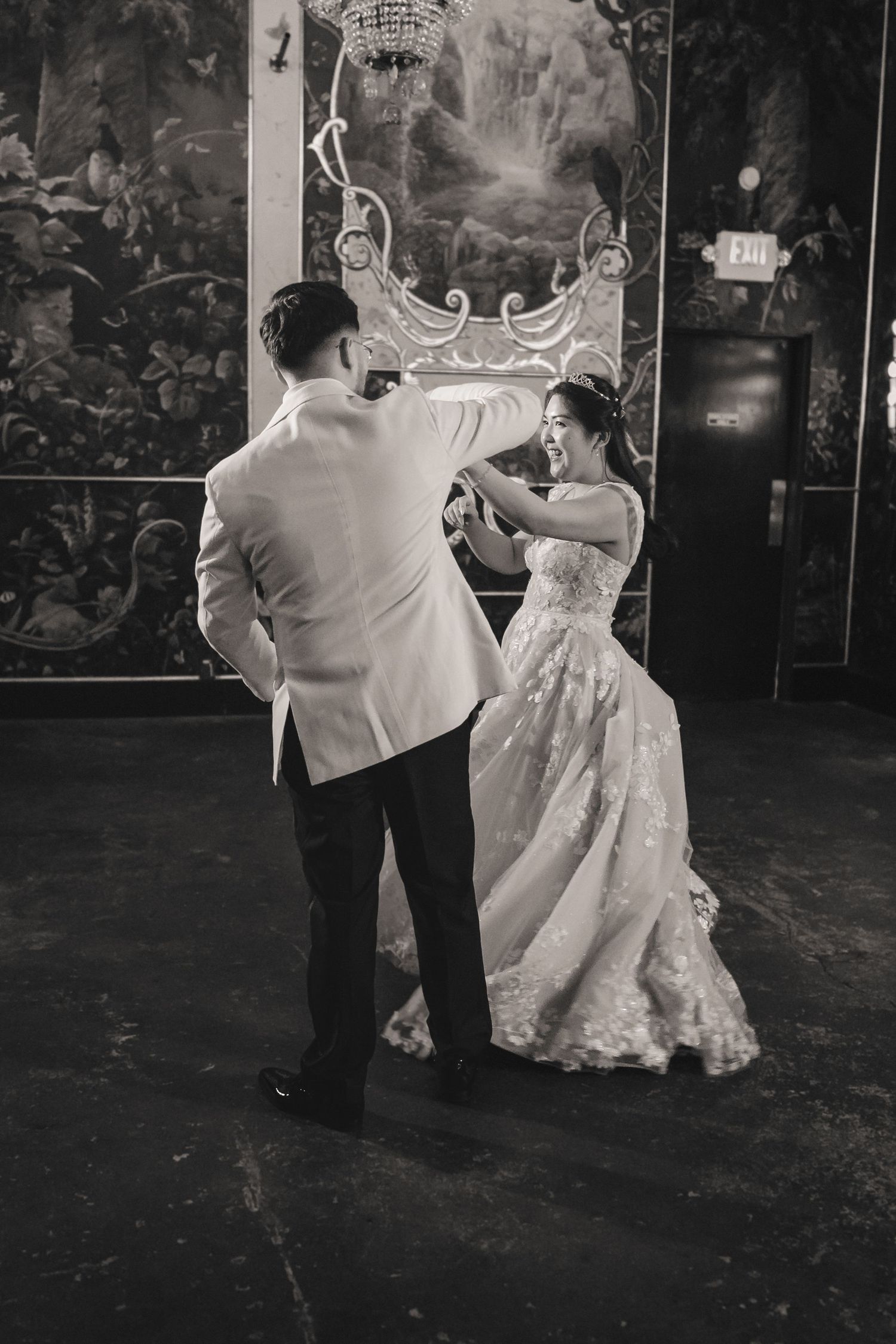 Black and white photo of a bride and groom sharing their first dance at an elegant wedding reception venue.