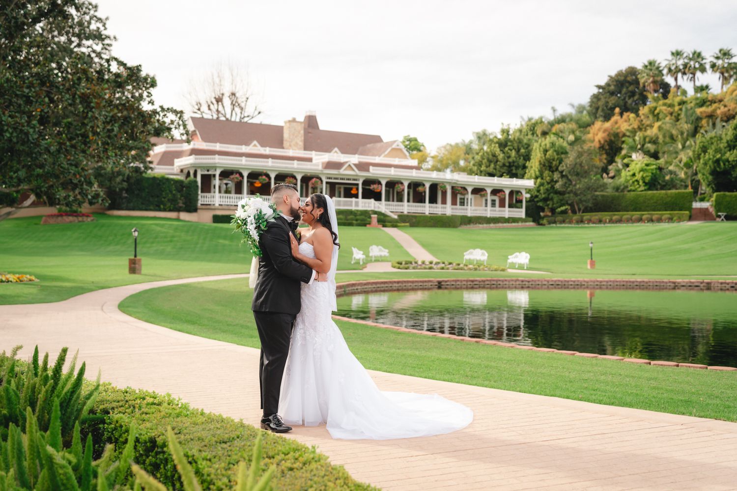 A wedding couple walks along a scenic path at a golf course with lush green landscaping and elegant architecture.