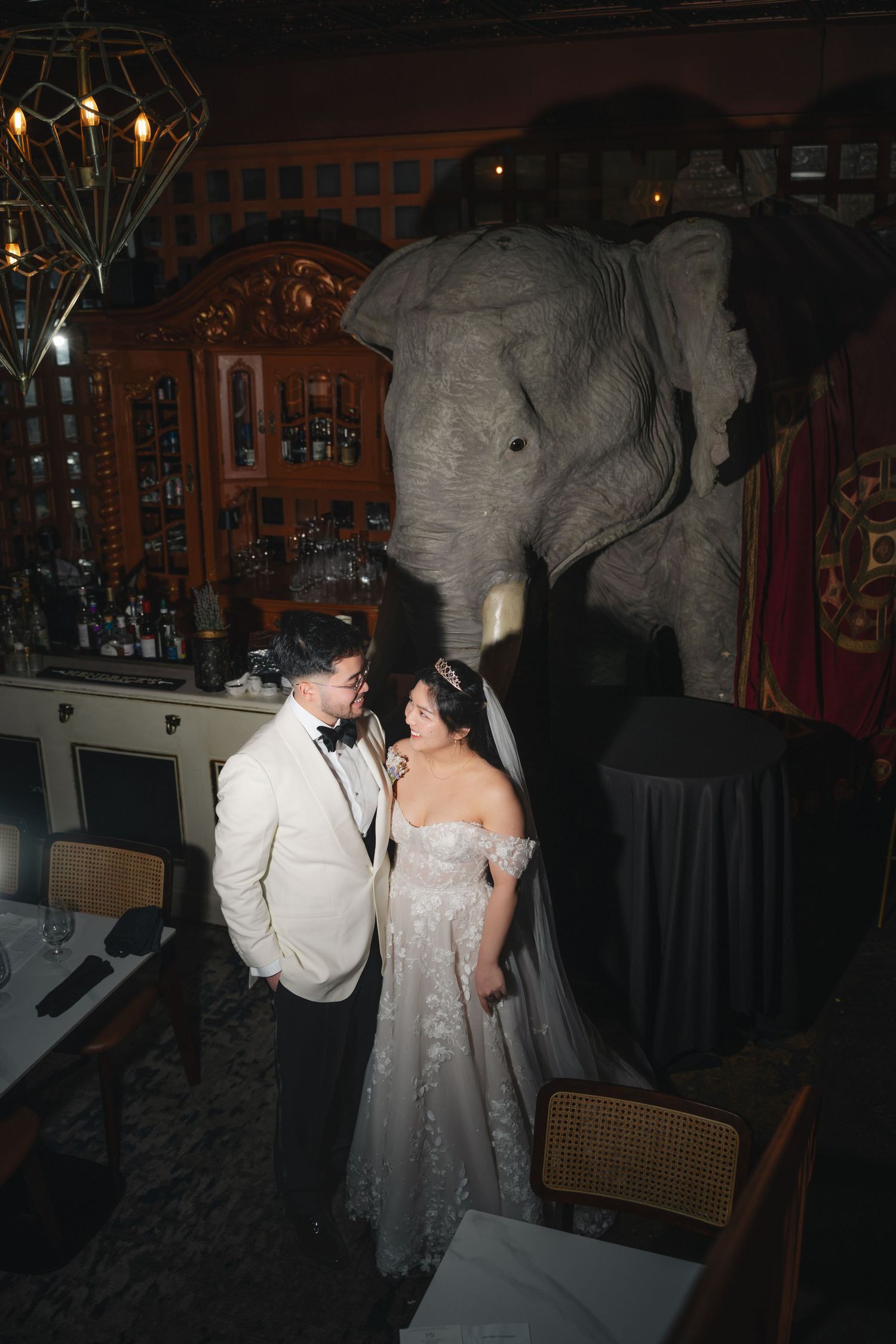 Bride and groom share a romantic moment in an elegant venue with a large elephant statue backdrop.