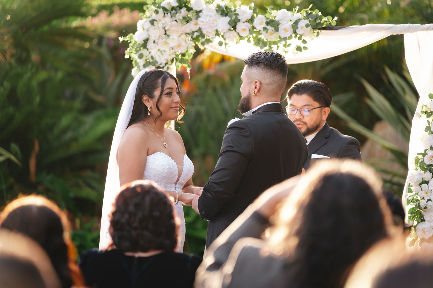 Outdoor wedding ceremony with floral arch and white chairs set up on manicured lawn.