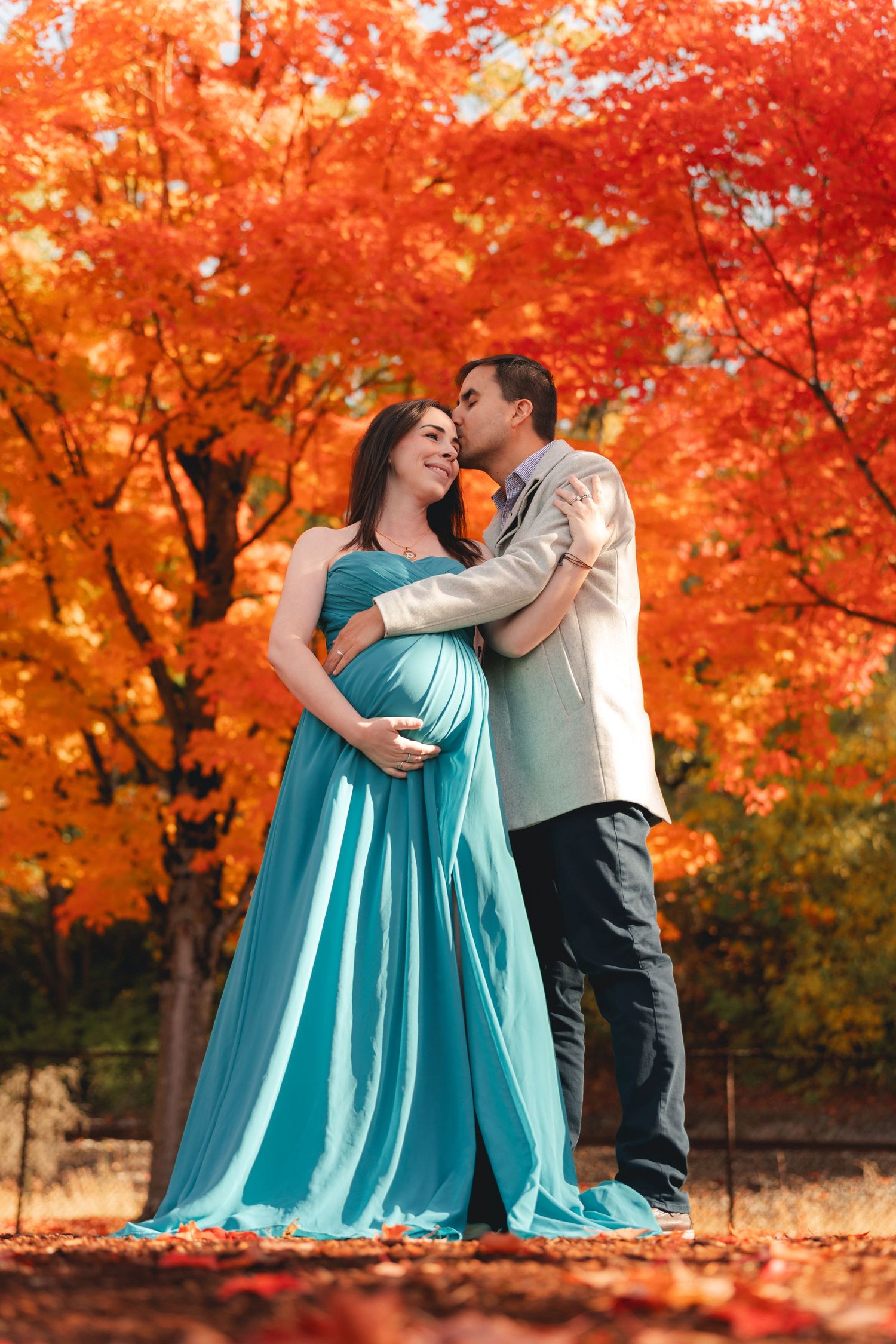 A couple embraces romantically under vibrant orange autumn maple trees in a park setting.