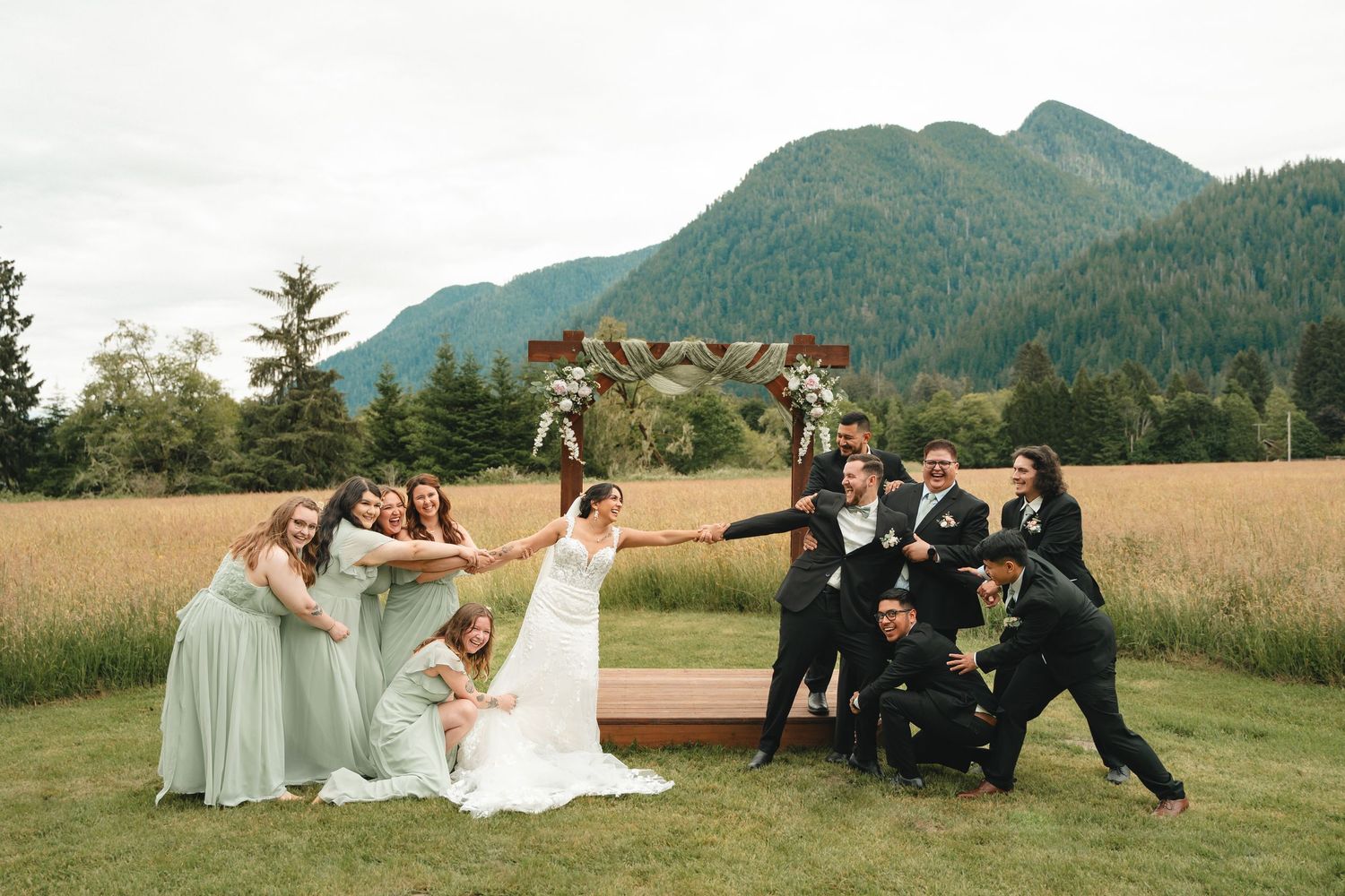 Wedding party poses playfully in a scenic mountain meadow at sunset.