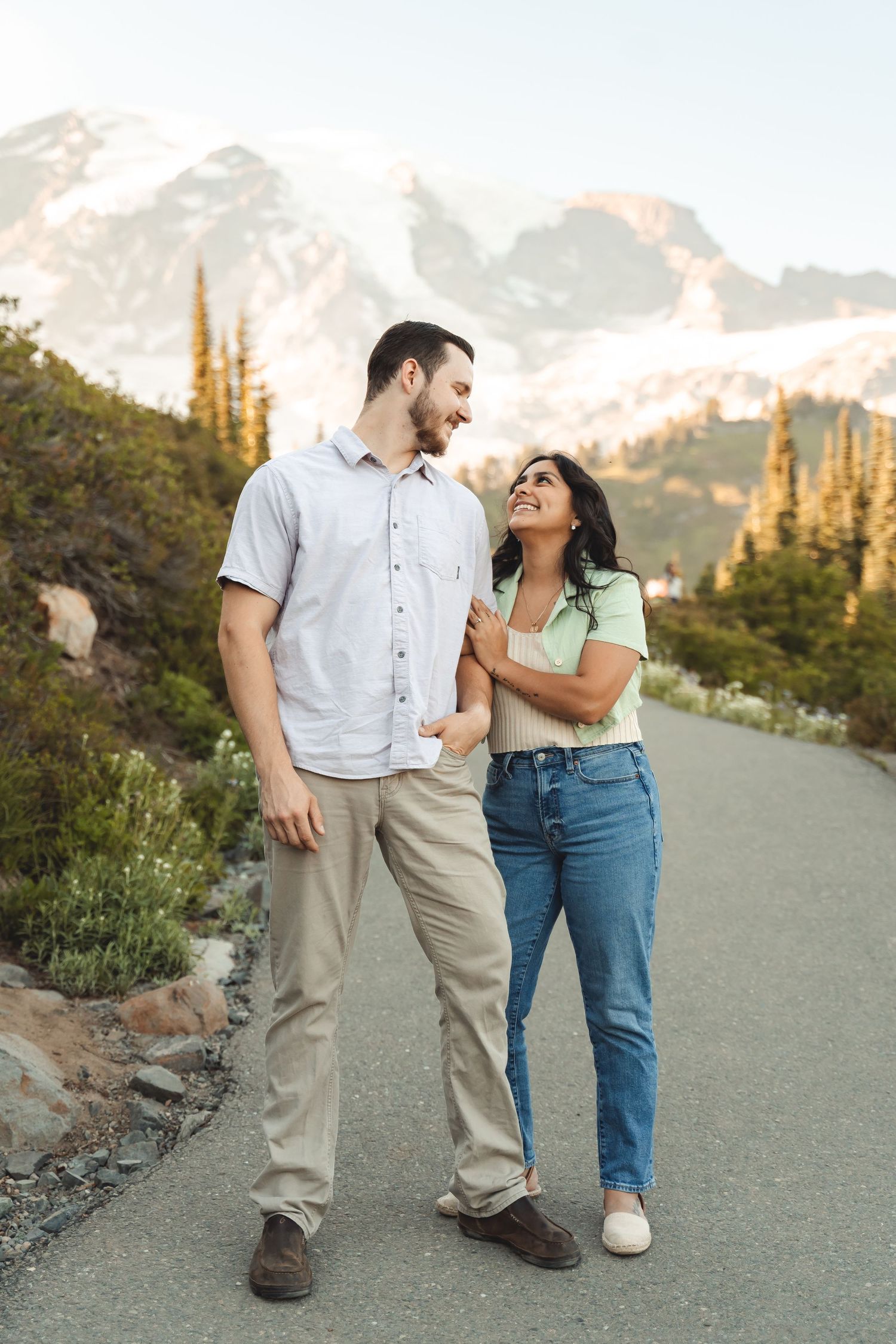 A couple shares a romantic moment while walking on a mountain trail during sunset.