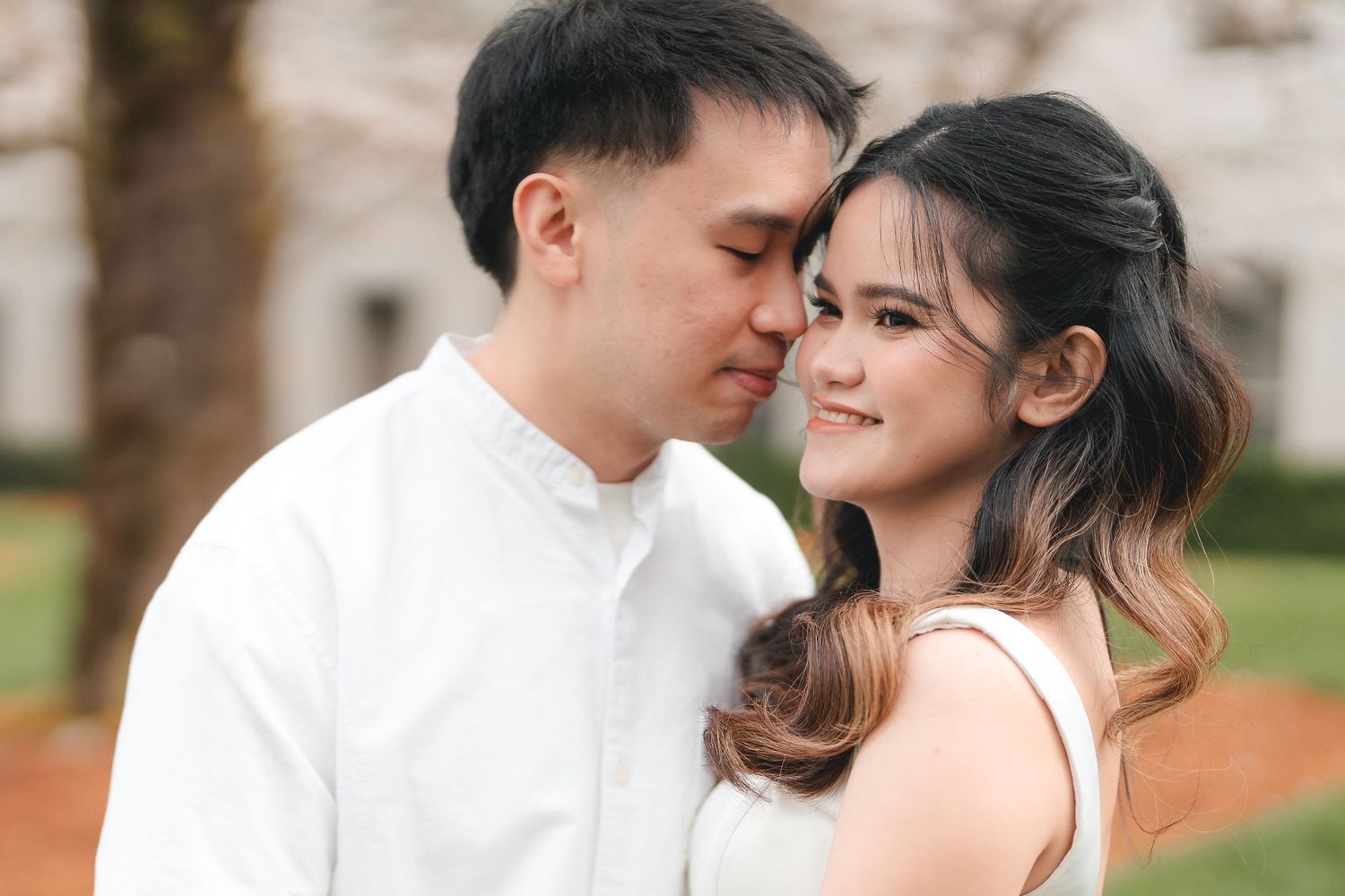 A romantic couple in white embraces during an outdoor photo session in a garden setting.
