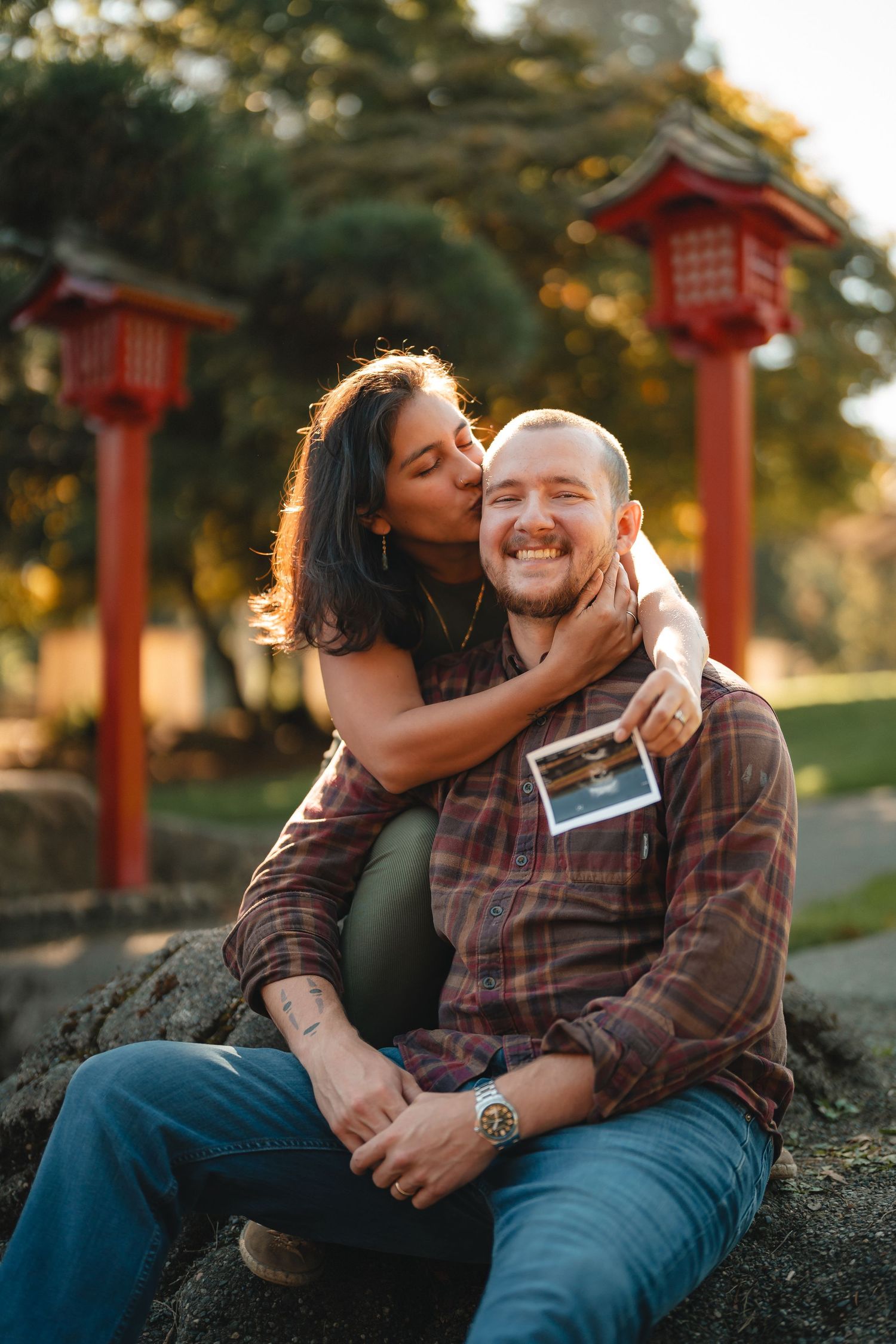 A couple shares tender moments in front of red Japanese-style lantern posts during a sunset photo session.