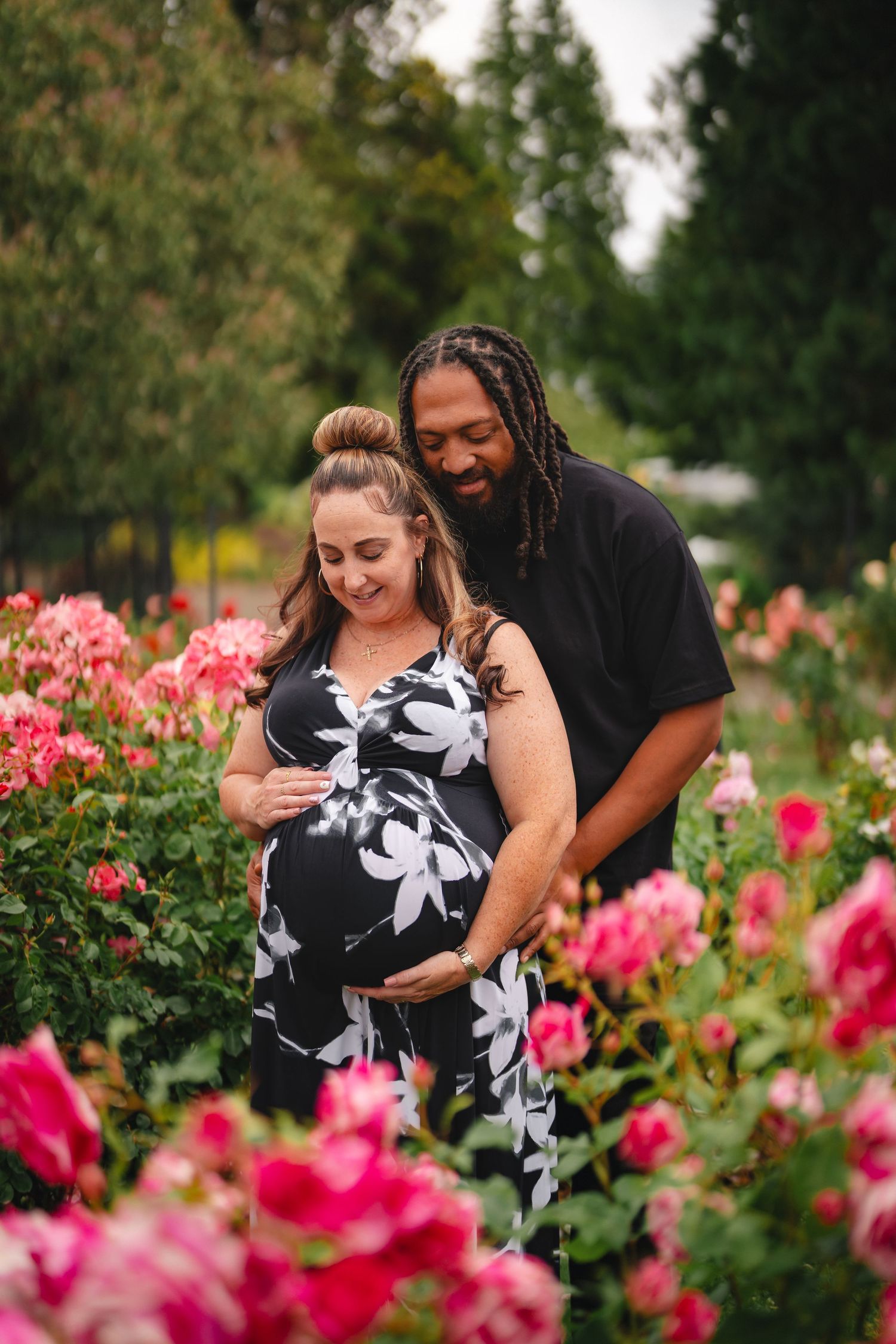 A couple shares intimate moments together in a garden with blooming pink roses on a summer day.