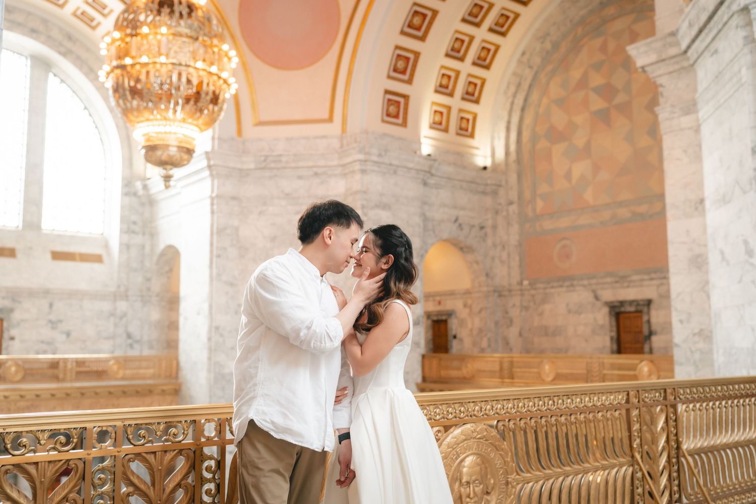 A romantic couple shares tender moments in an ornate palace hallway with elegant chandeliers and stone architecture.