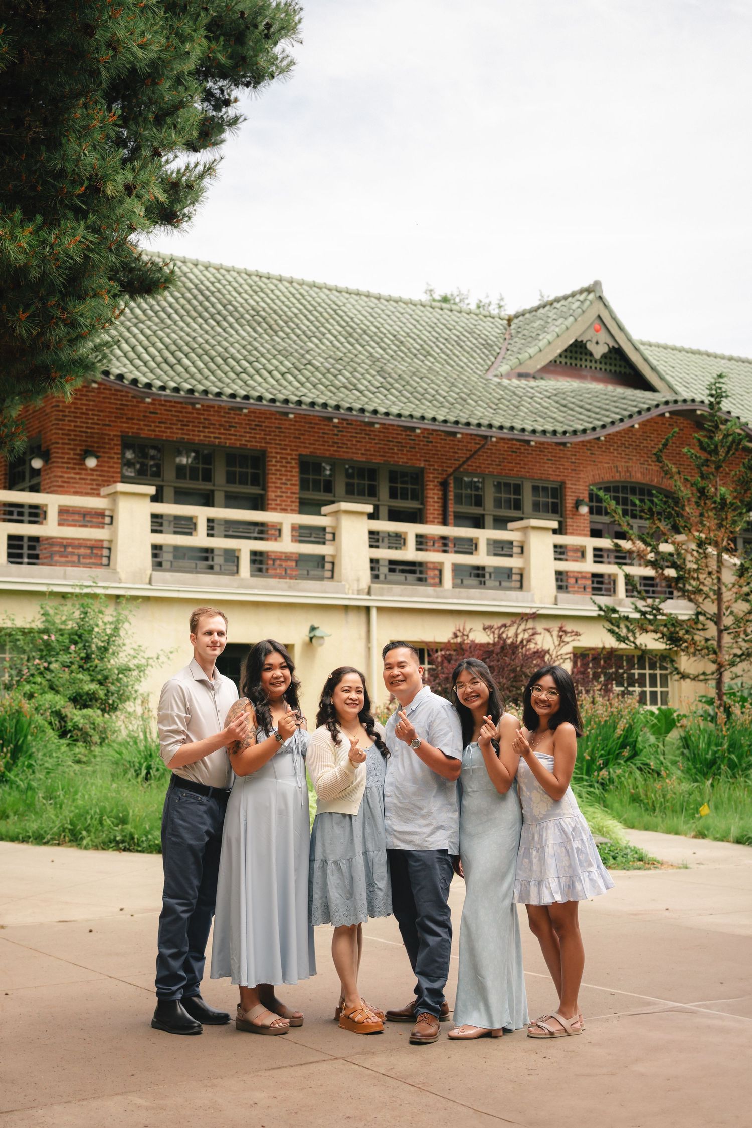 A group of friends pose together in front of a traditional Asian-style building with green tiled roof and red walls.