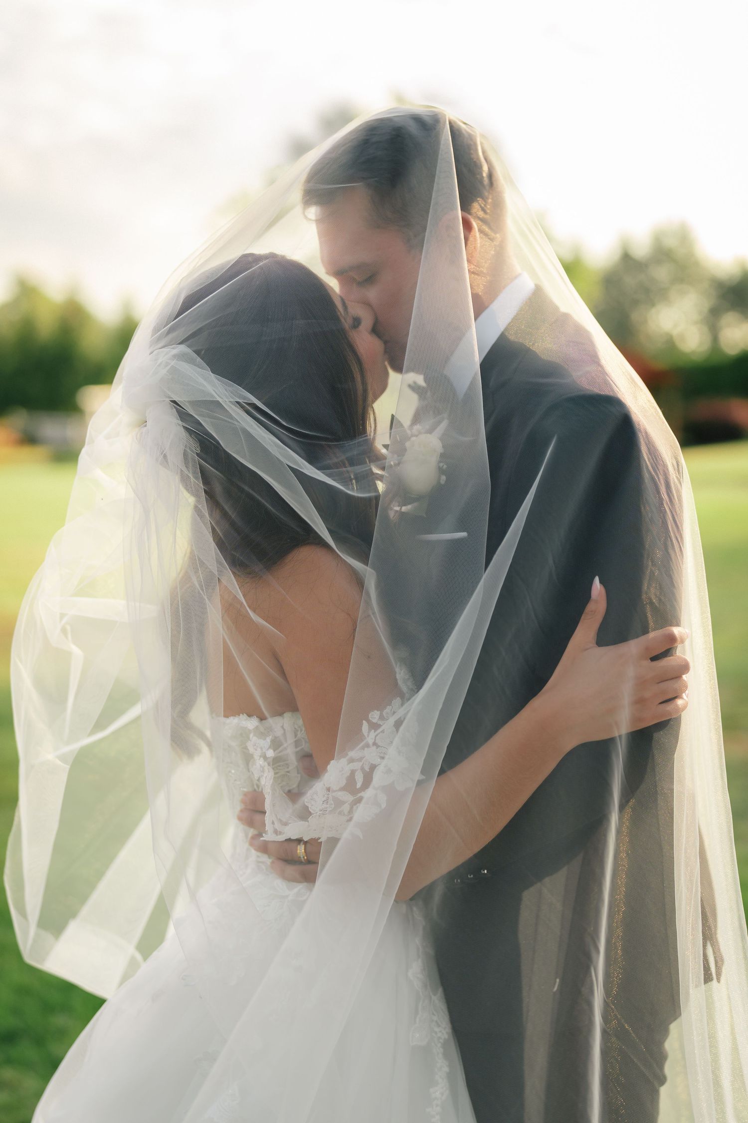 A romantic wedding photo series showing a couple embracing under a flowing white veil in an outdoor garden setting.
