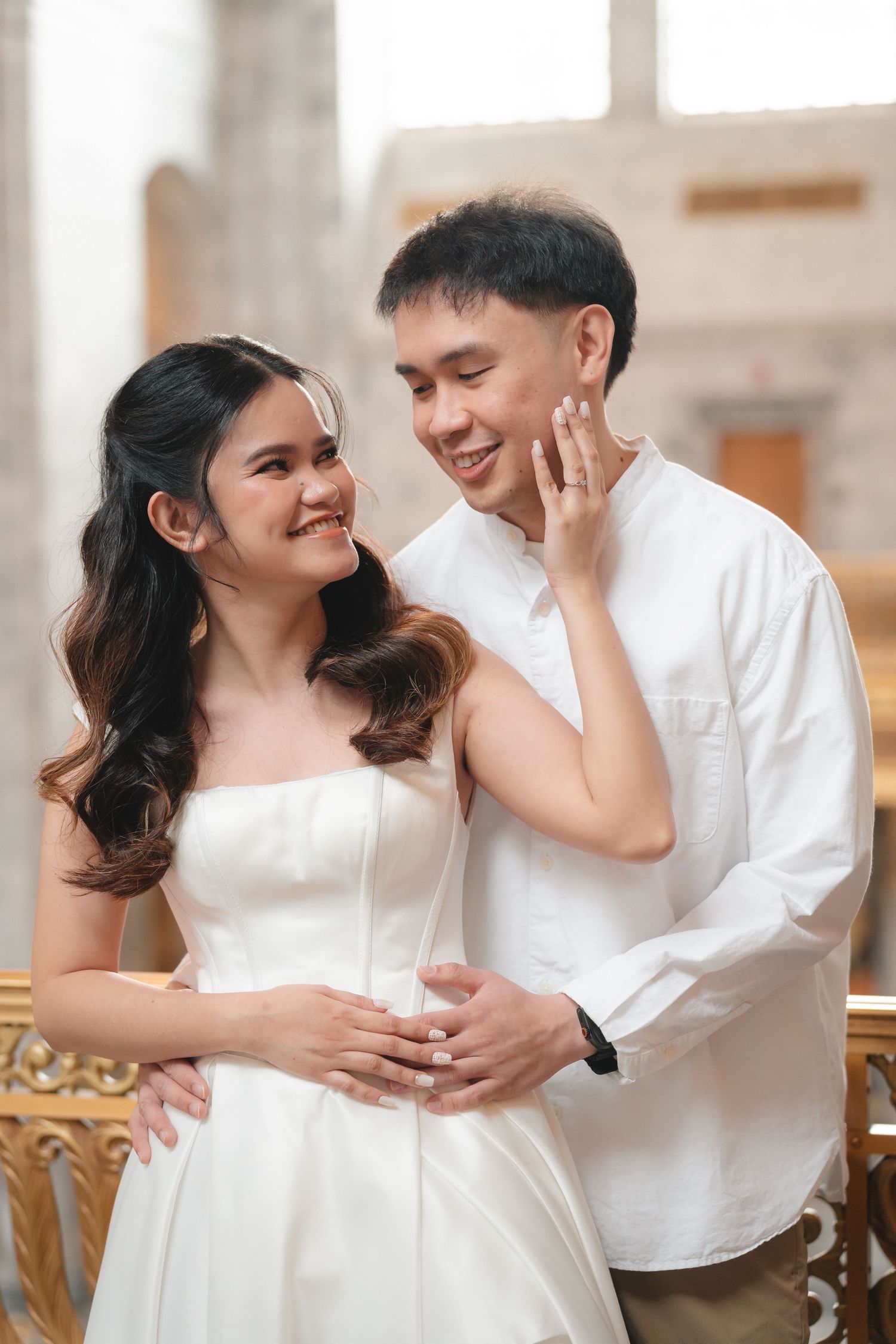 A couple in white outfits share intimate moments while sitting together in a bright indoor setting.