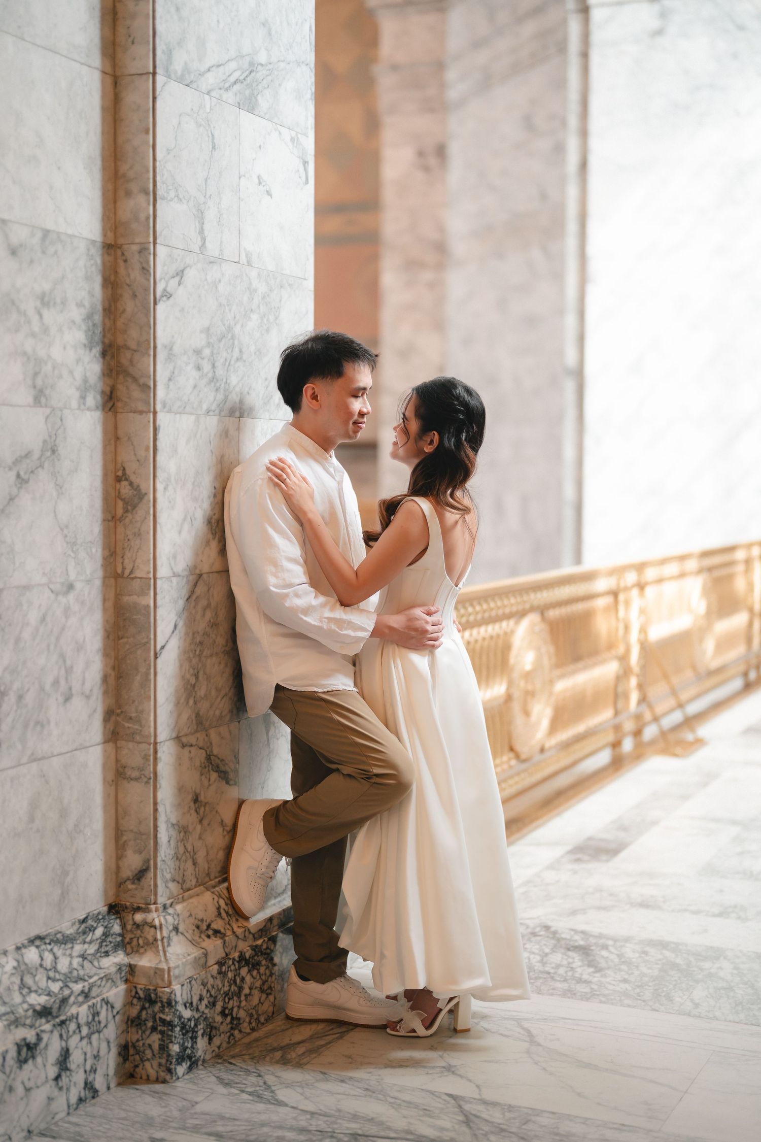 A romantic couple shares tender moments in an elegant archway with marble columns and warm sunlight.