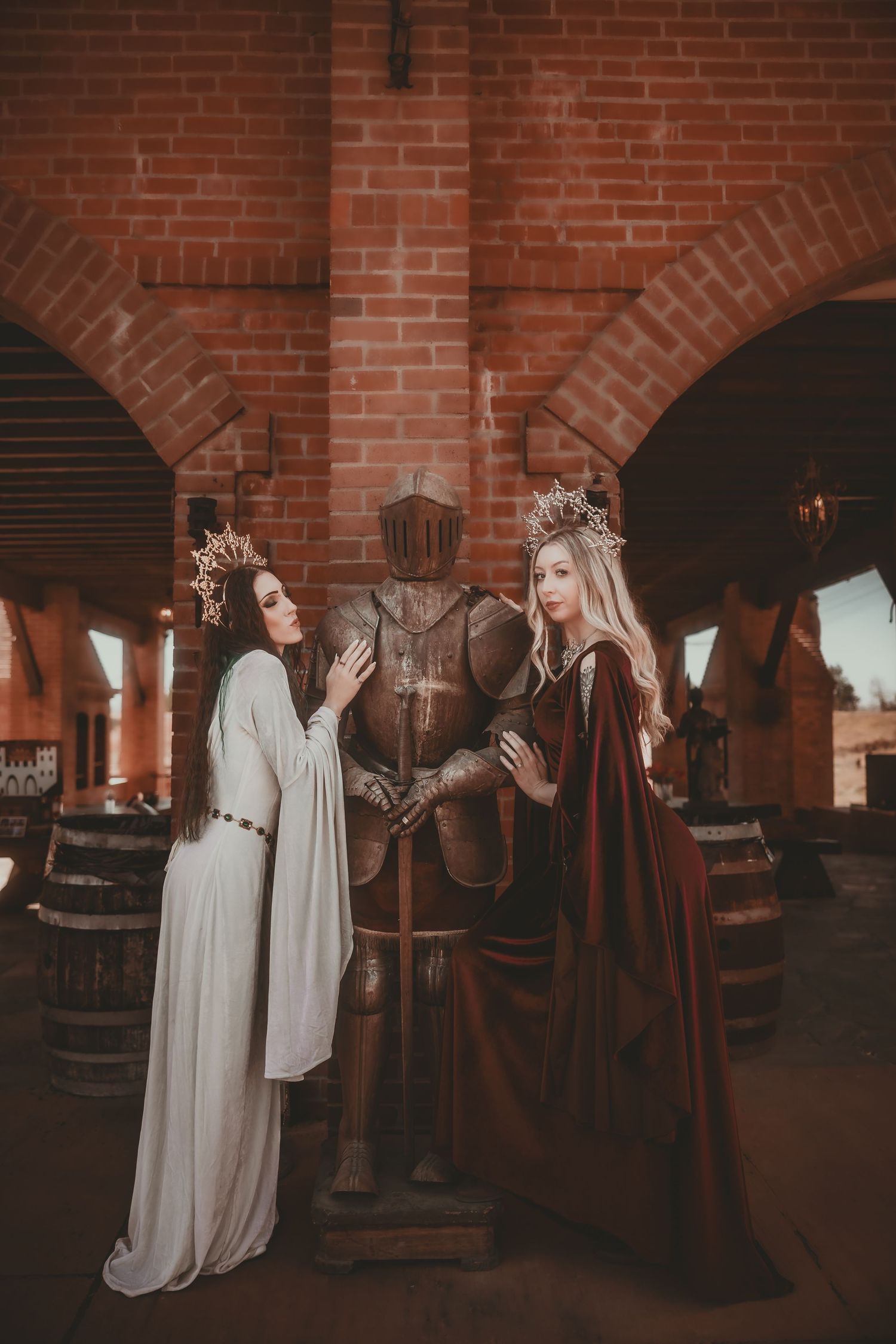Two medieval queens in crowns and gowns flank an armored knight statue in a brick castle setting.