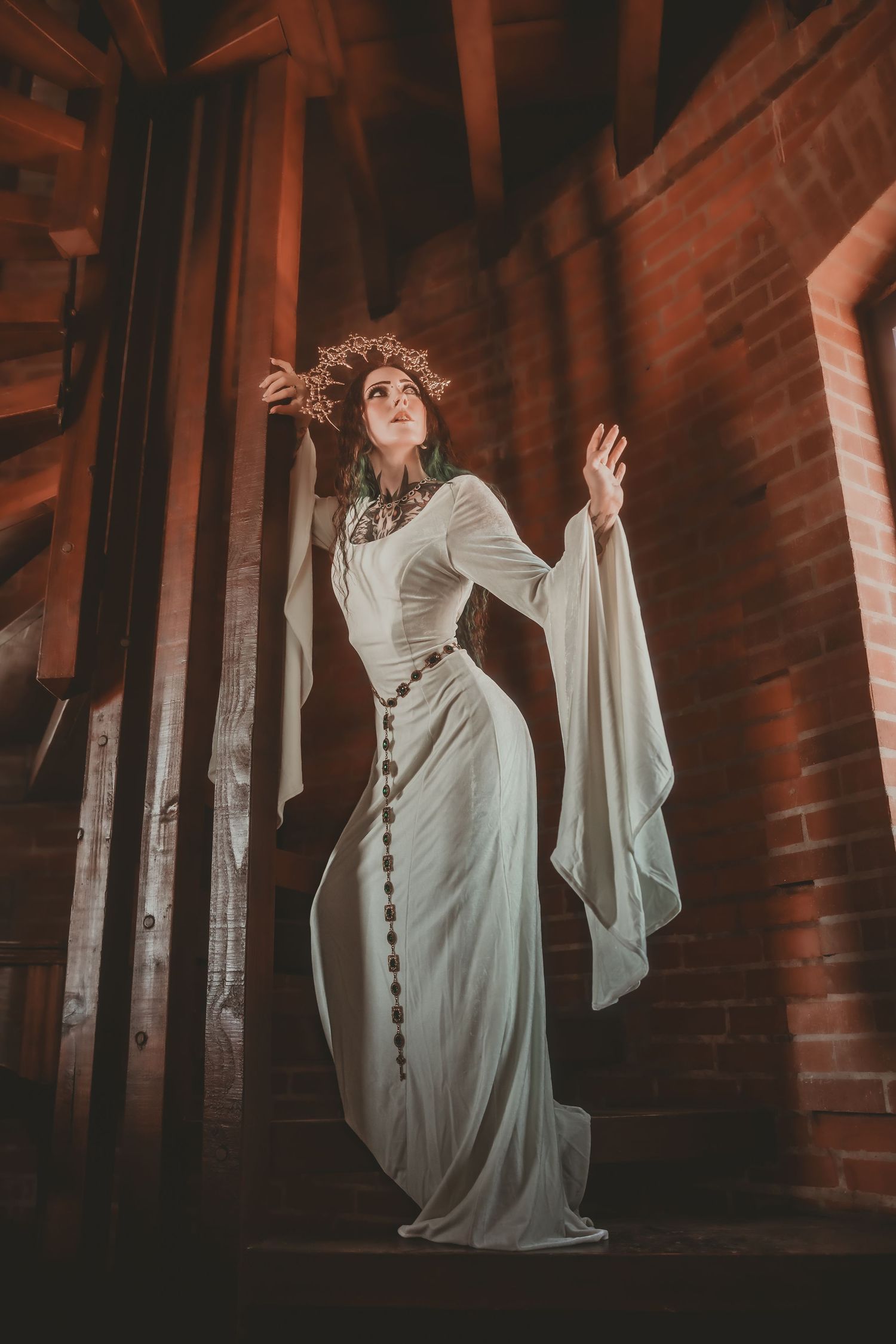 Woman in white medieval gown and floral crown poses dramatically in rustic brick castle stairway.