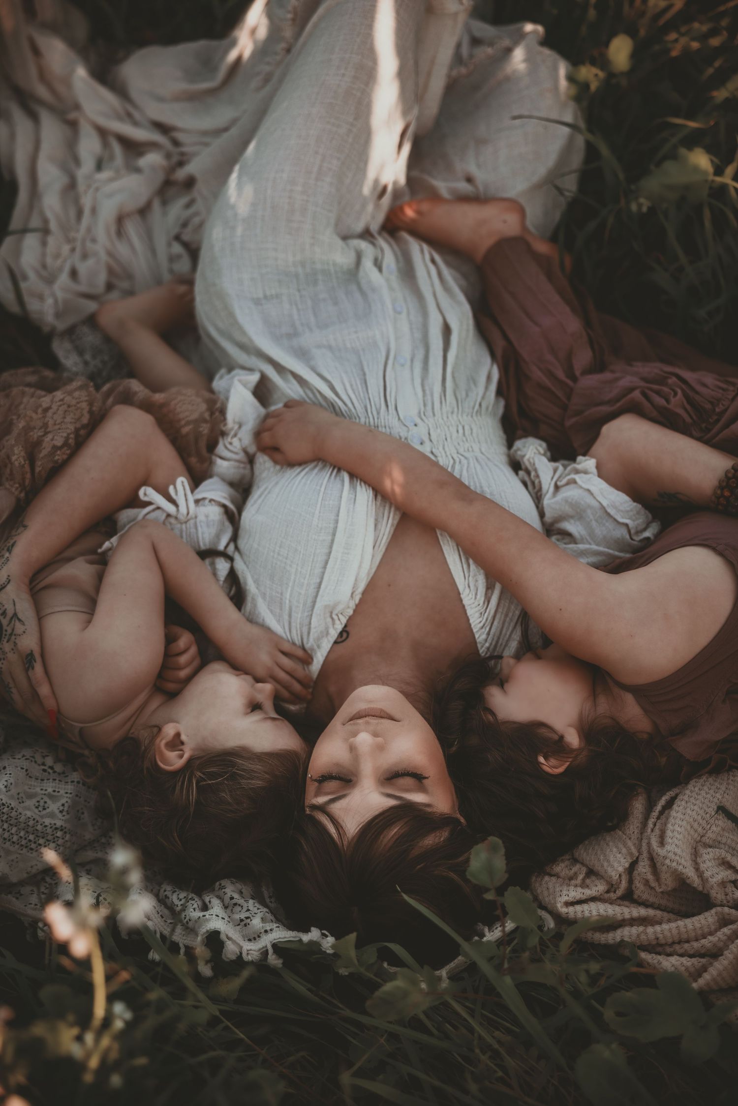 Two people lying down in white clothing on grass and wildflowers in an artistic outdoor portrait.