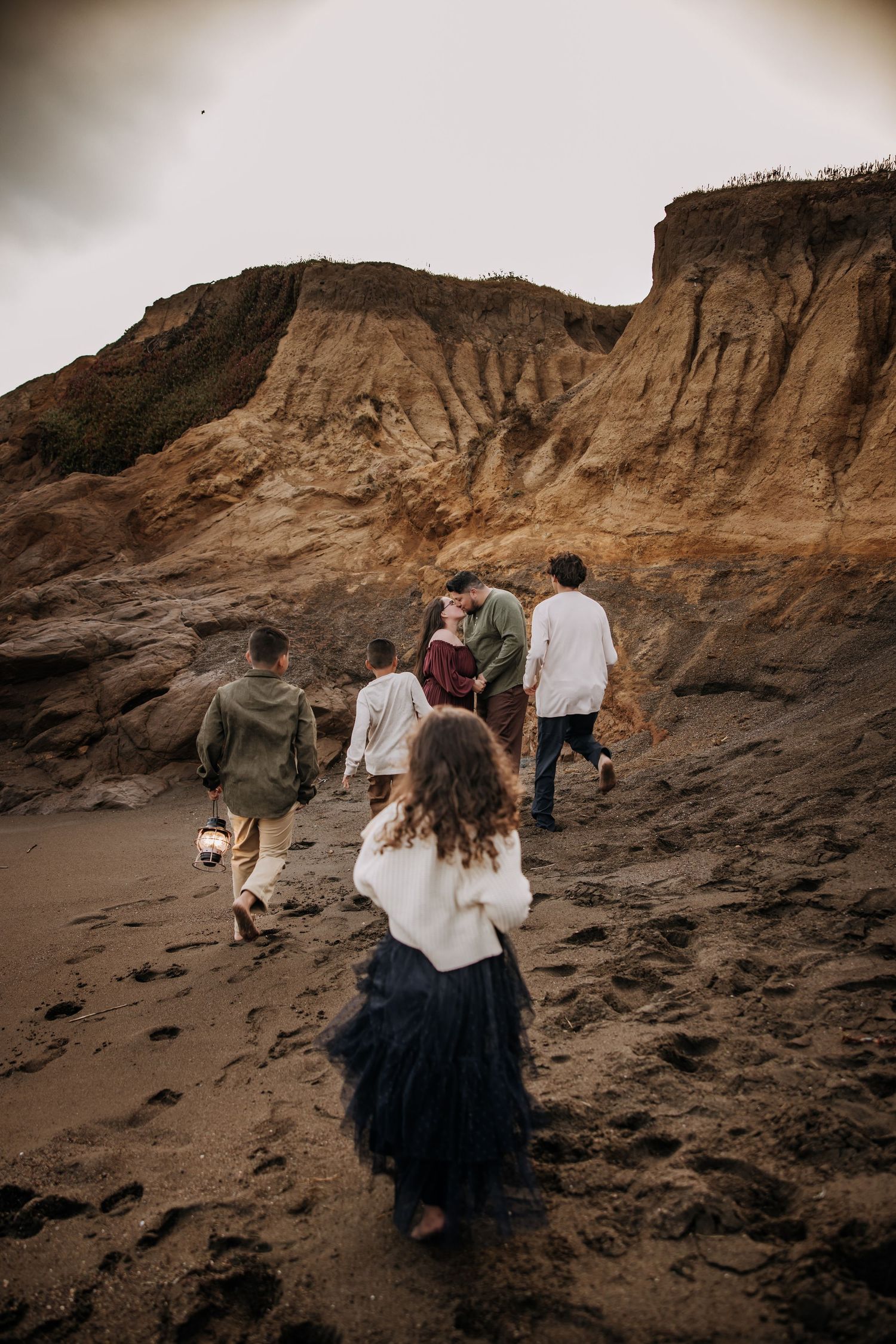 Group walking along rugged coastal cliffs at sunset with dramatic rock formations in the background.