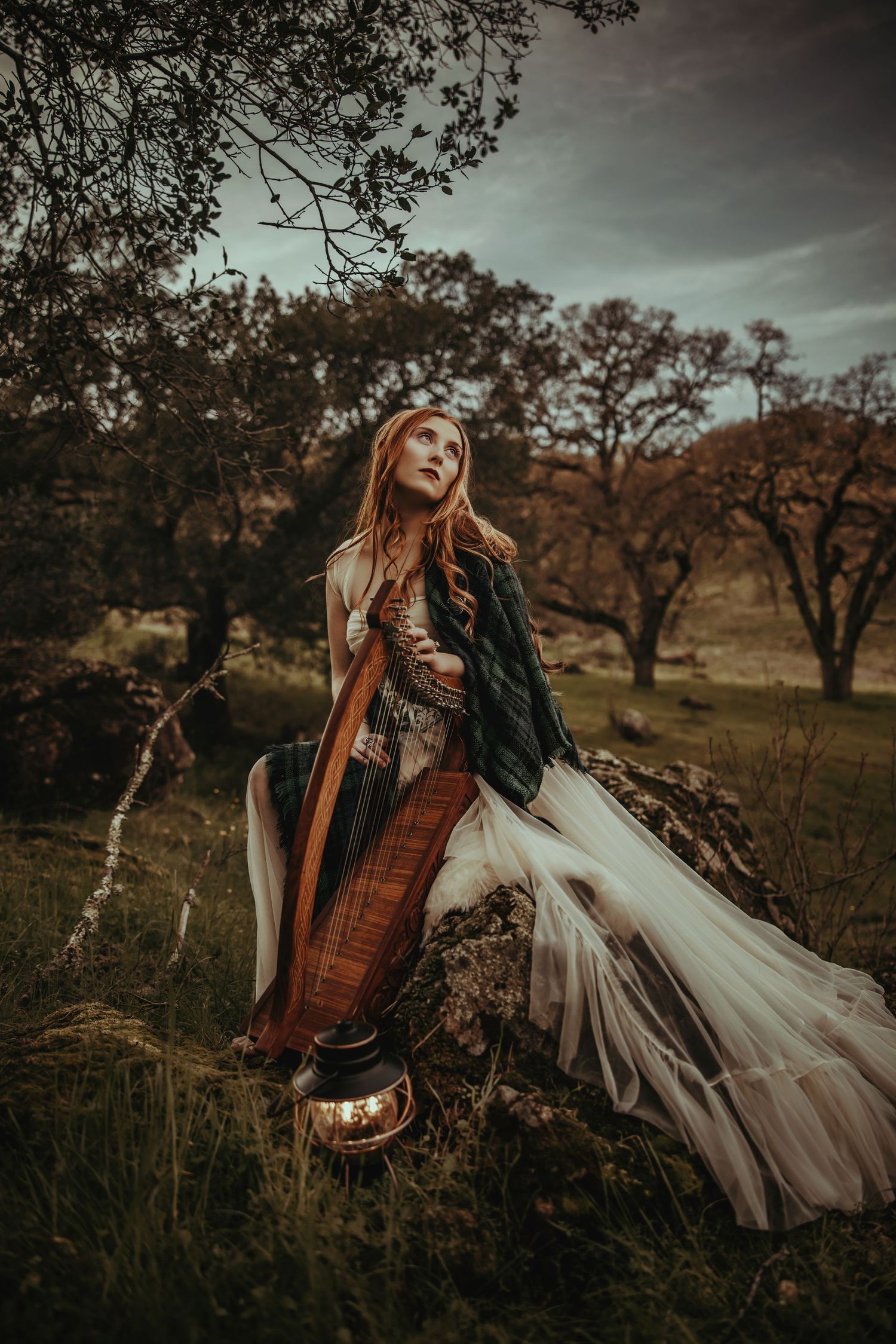 A figure in a flowing white dress and brown jacket twirls dramatically in an autumn field at sunset.