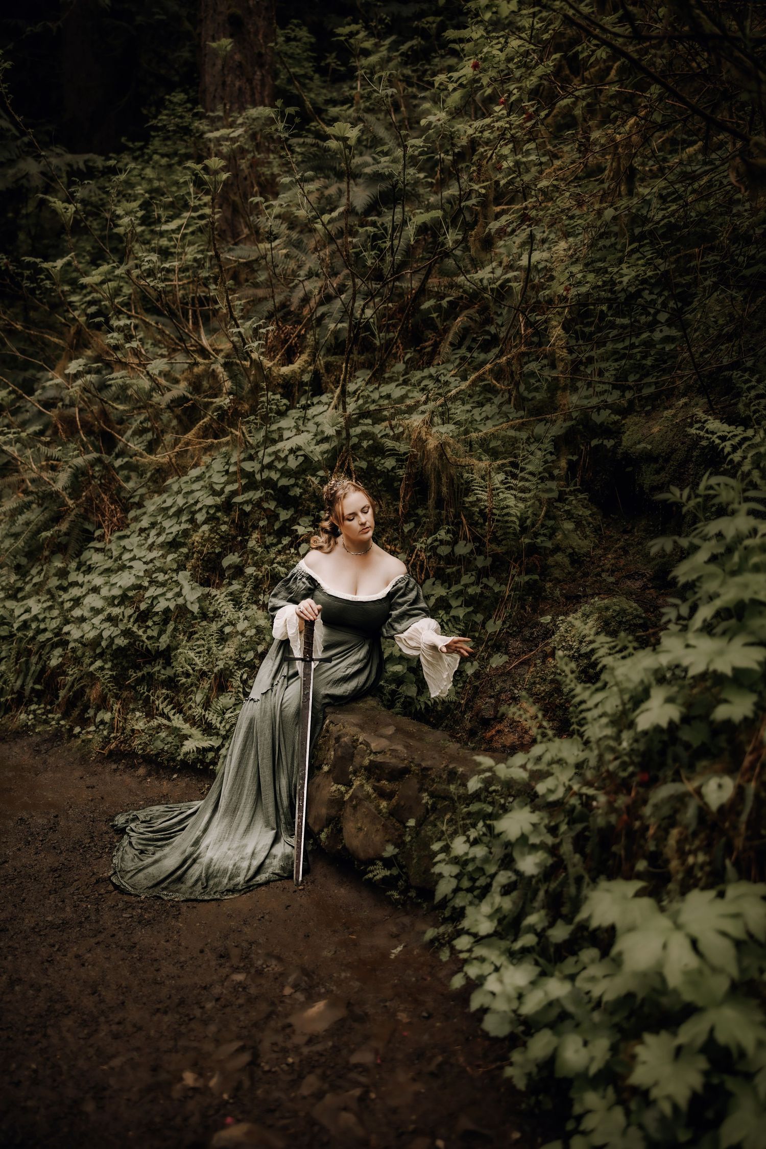 A person in a flowing vintage dress poses gracefully on a forest path surrounded by lush greenery and ferns.
