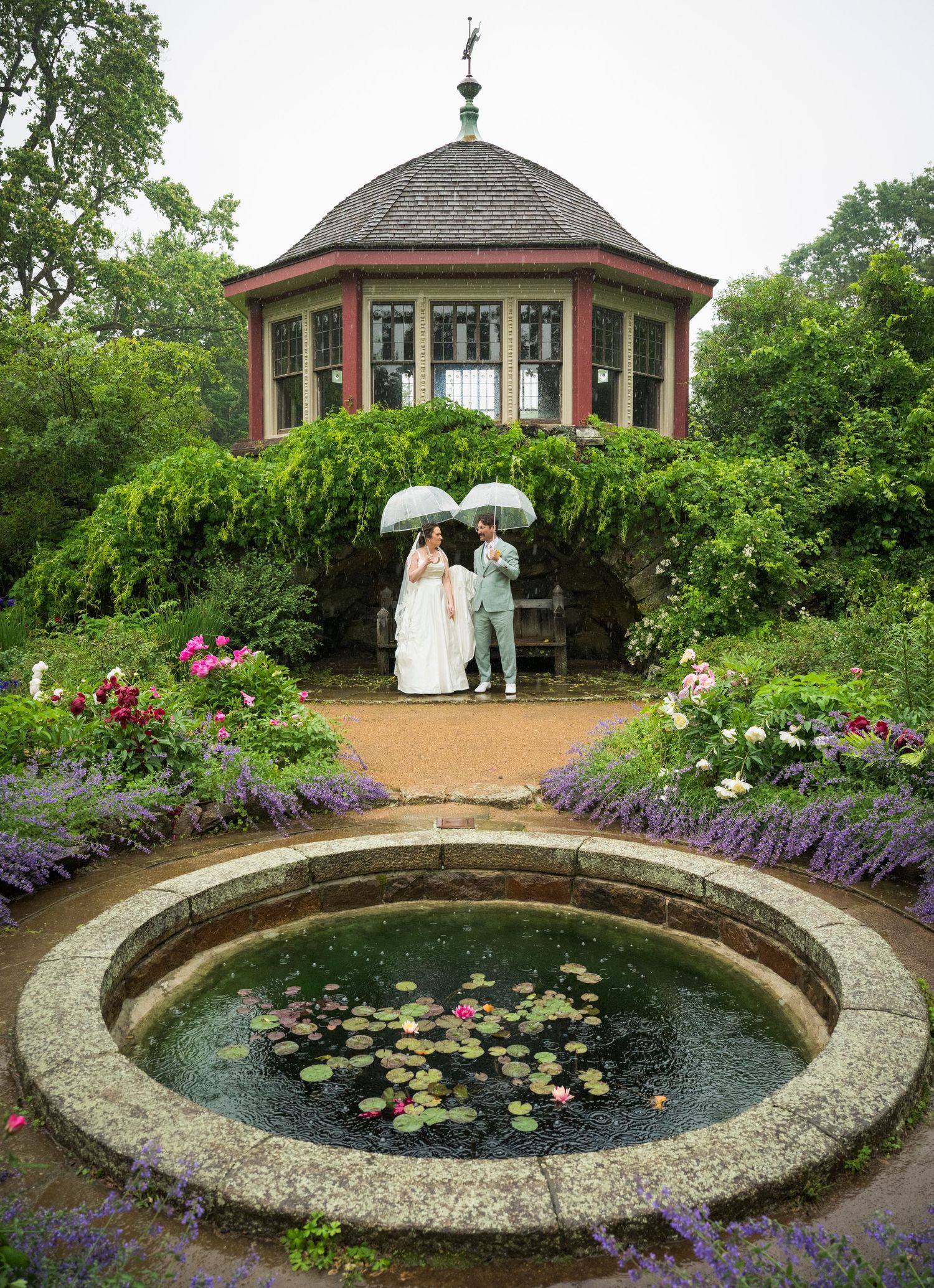 A series of garden gazebos with a circular lily pond surrounded by purple flowers and lush landscaping.