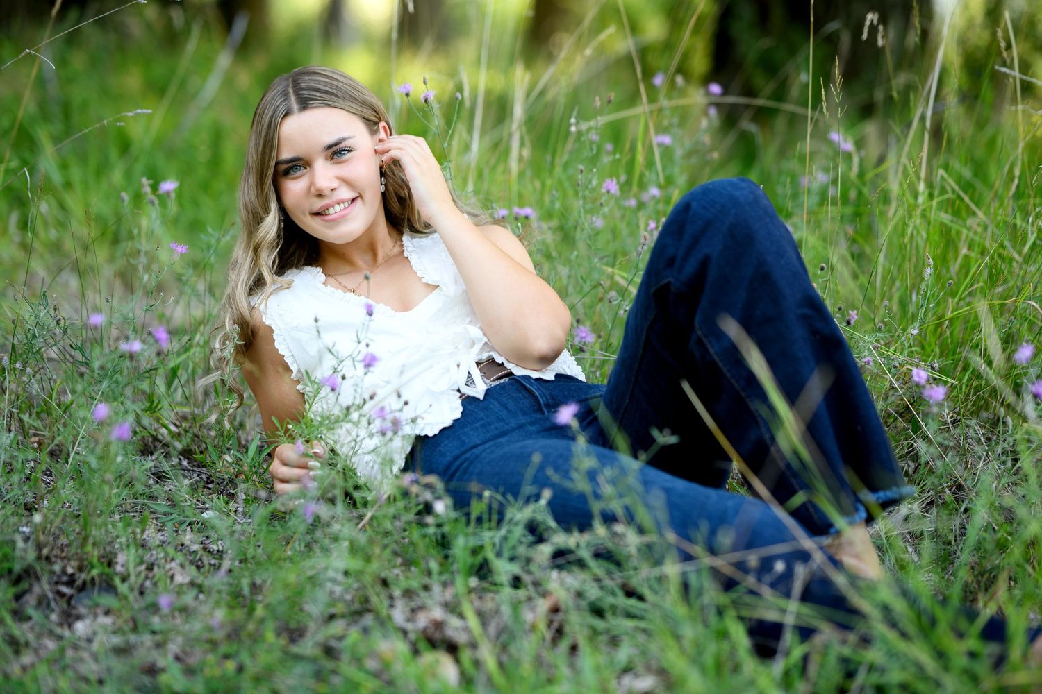 A person in blue jeans and a floral top lies in a grassy meadow on a sunny summer day.