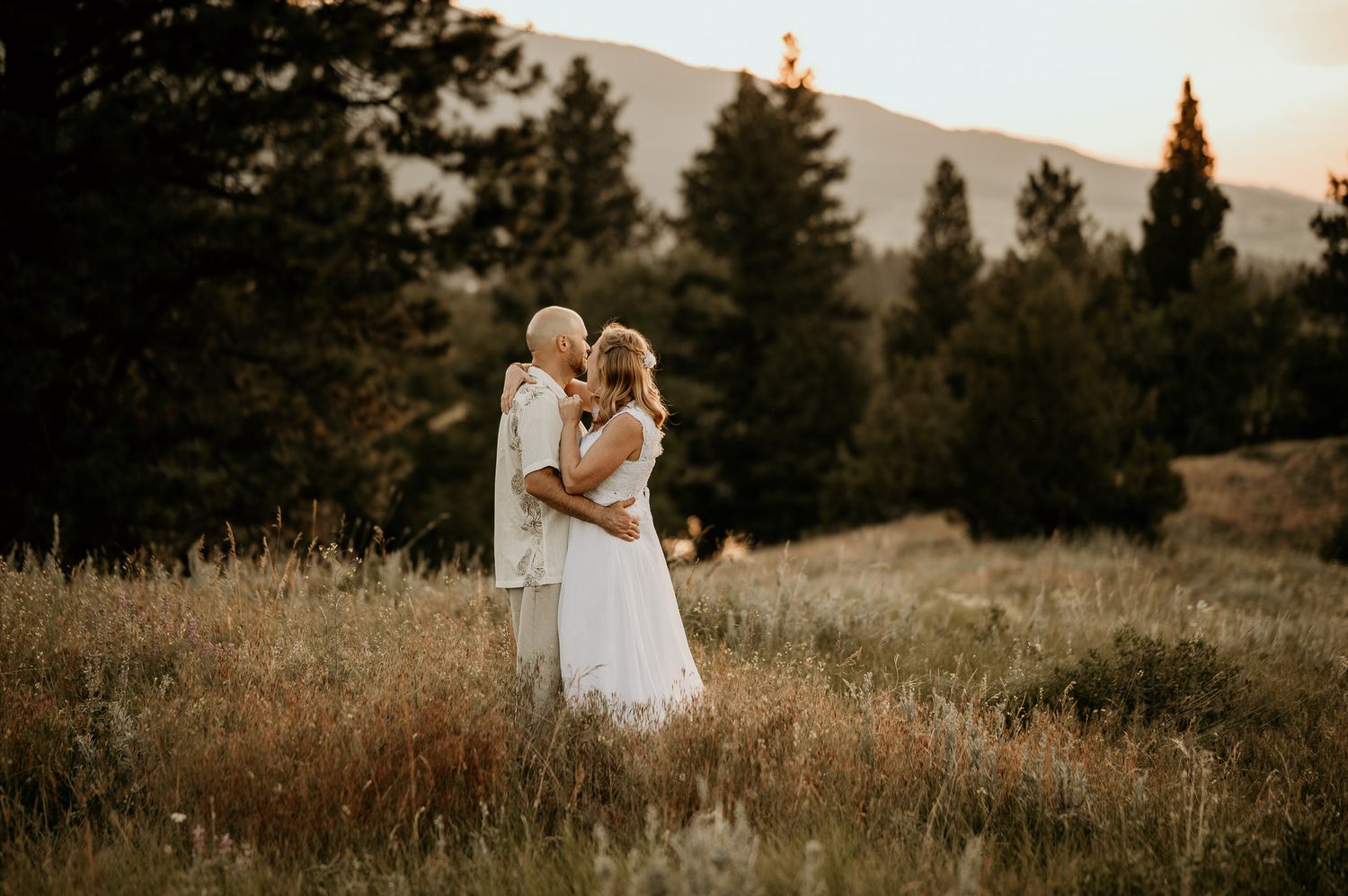 Couple embraces in mountain meadow during golden hour sunset.