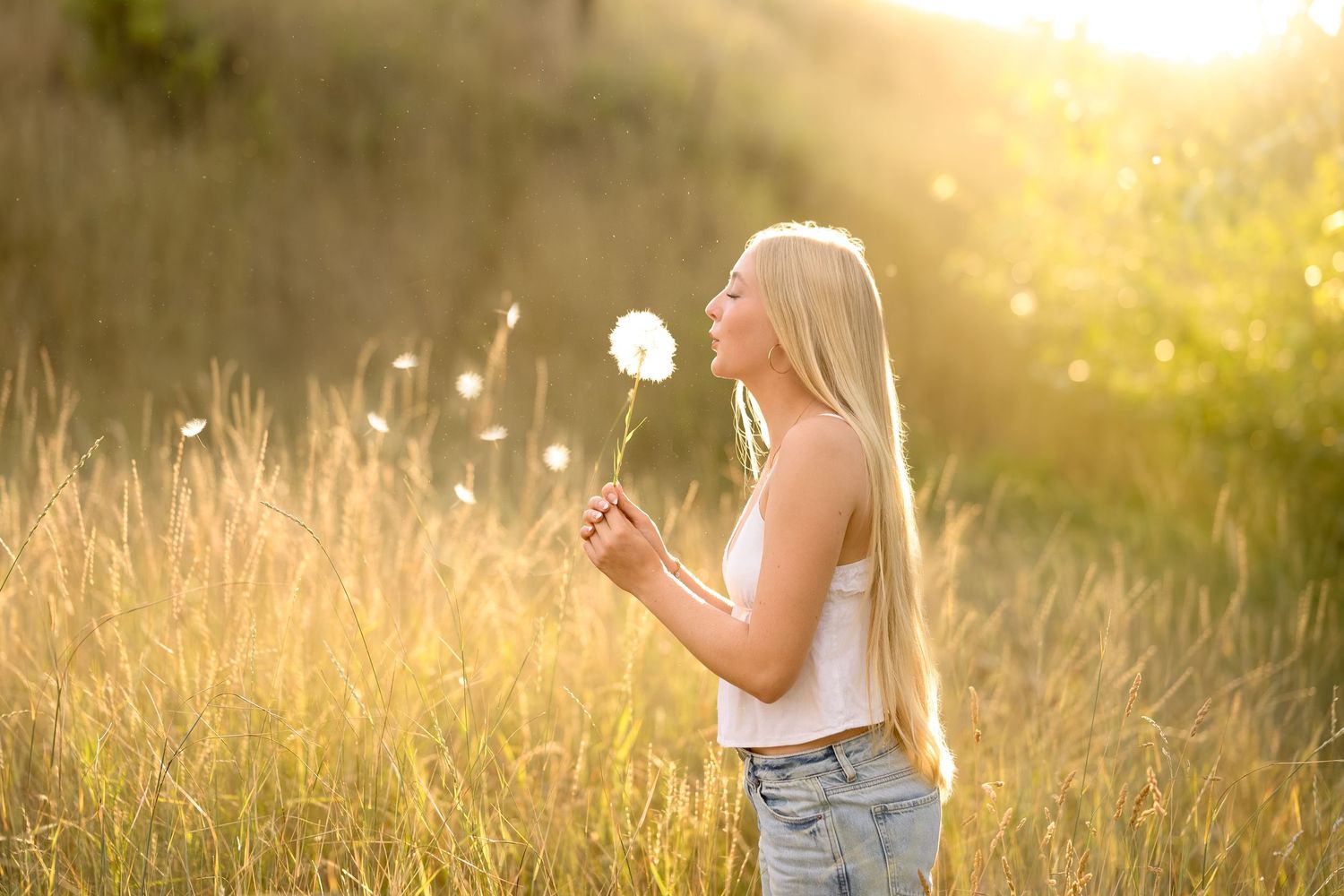 A person walks through a golden sunlit meadow at sunset wearing a white top and jeans.