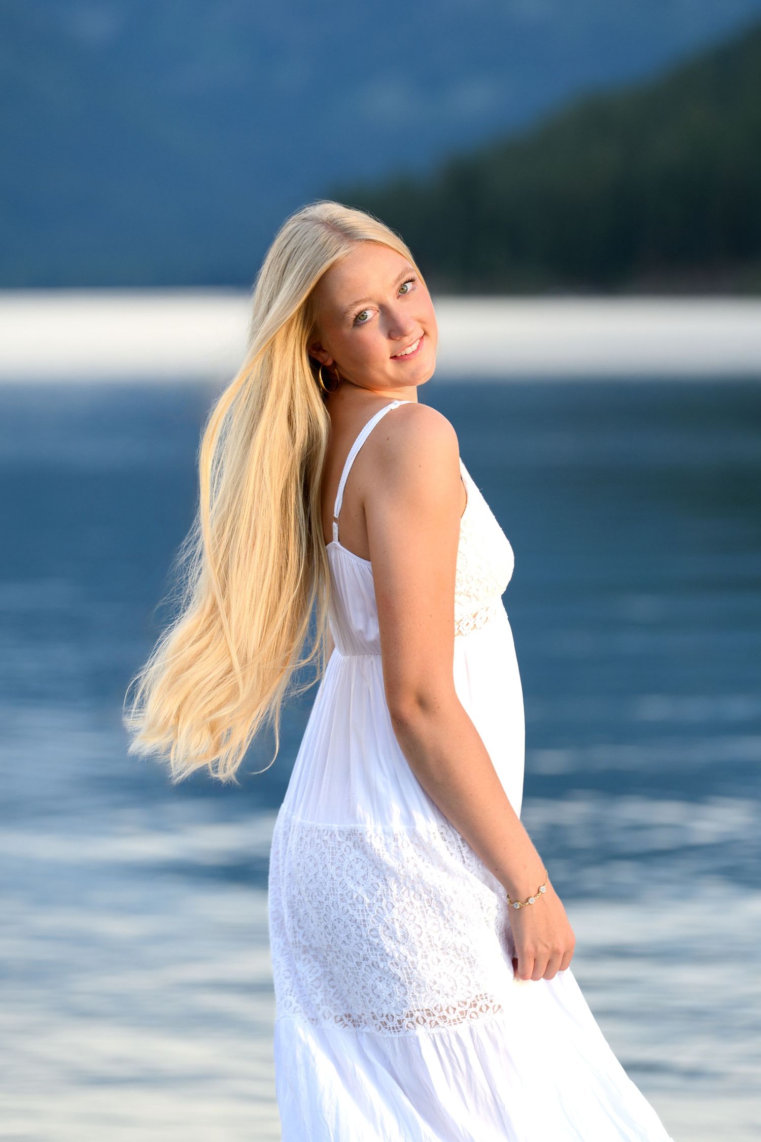 A woman in a flowing white sundress twirls joyfully on a beach with the ocean in the background.