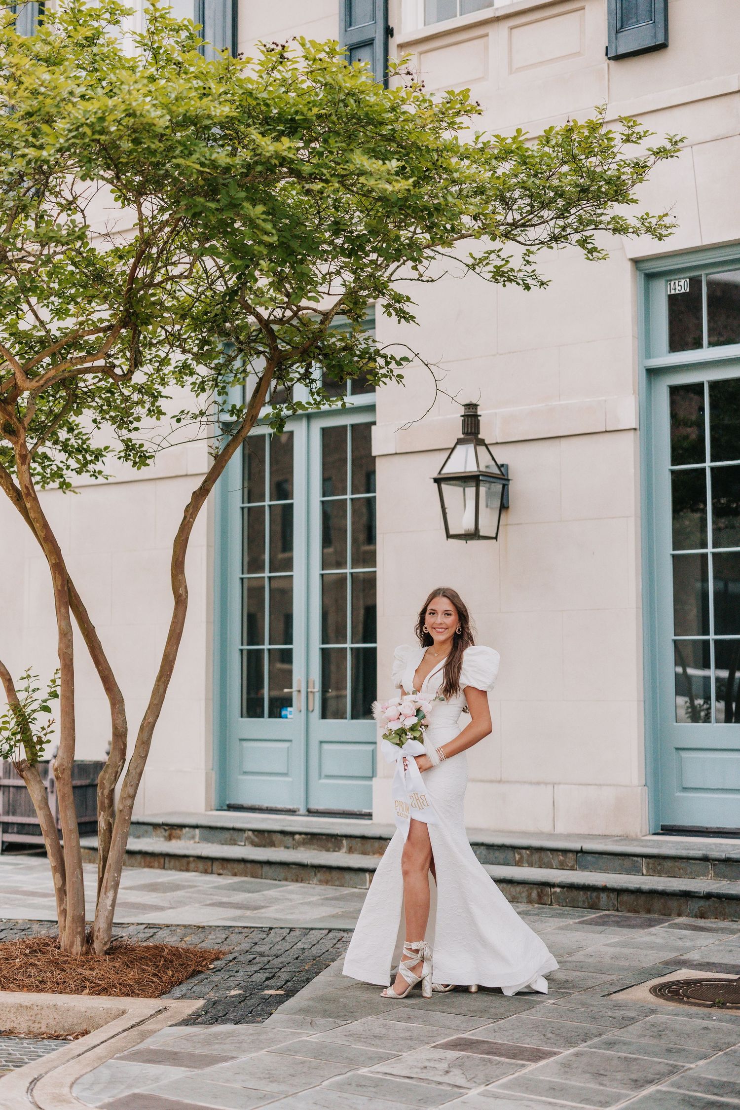 Woman in flowing white dress twirling outside elegant building with blue doors and windows.