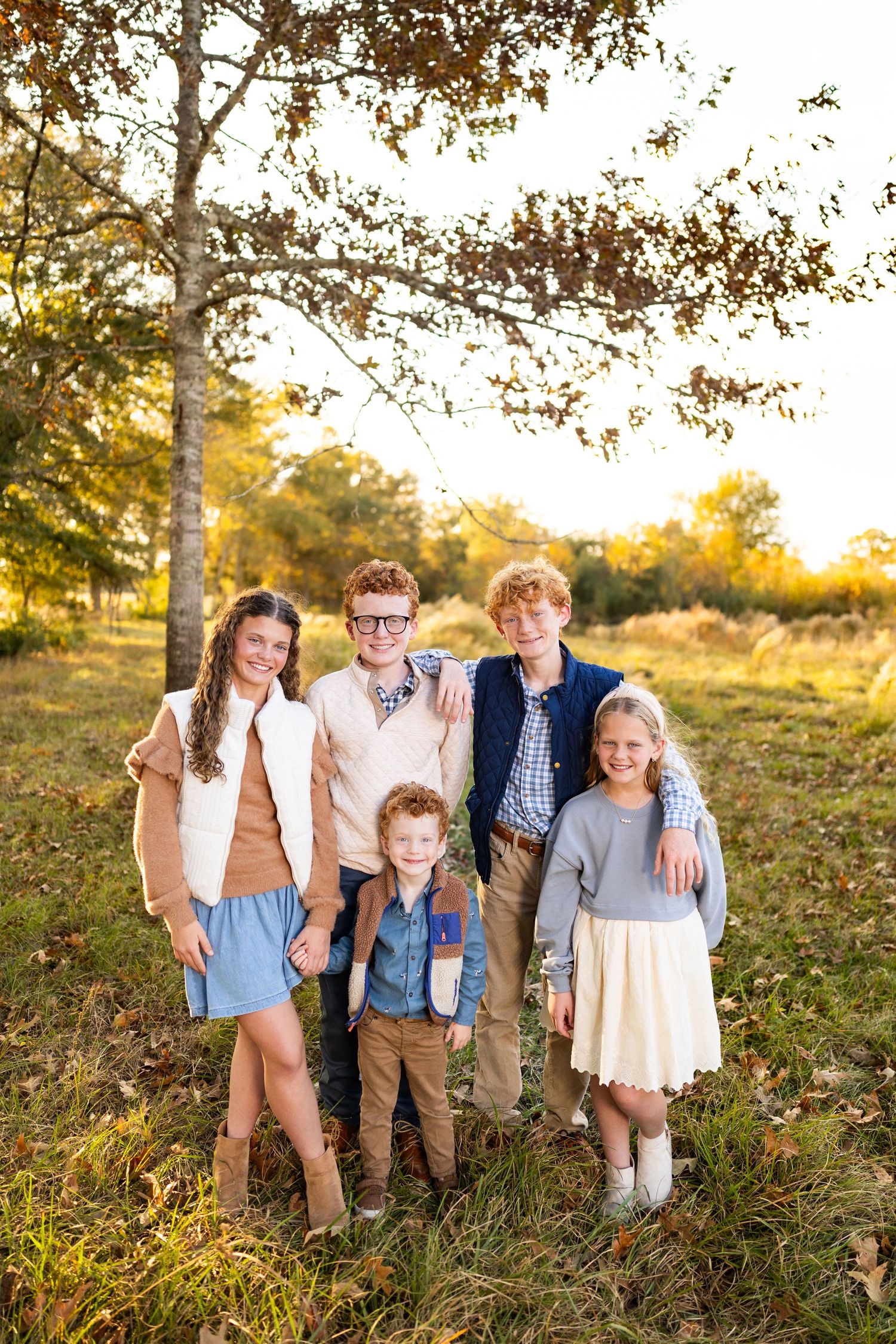 Group portrait in autumn setting with golden sunlight filtering through trees in background.