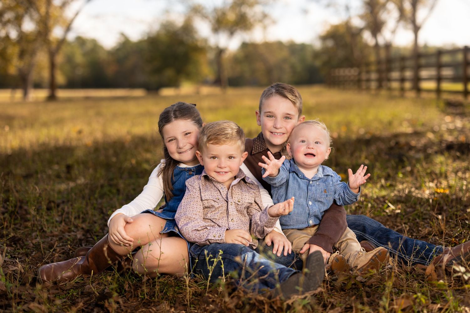 Four young children sit together on grass during golden hour in rural setting.