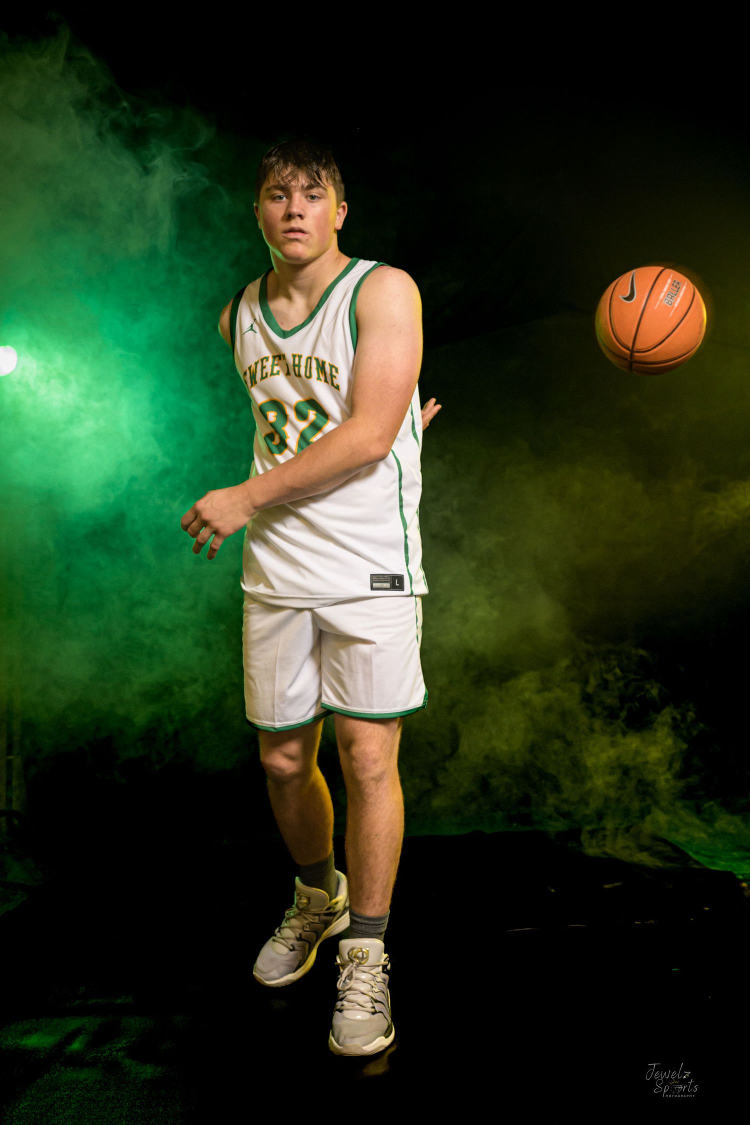 Teen basketball player in green and white number 82 jersey posing with Nike ball in dramatic smoky studio lighting.
