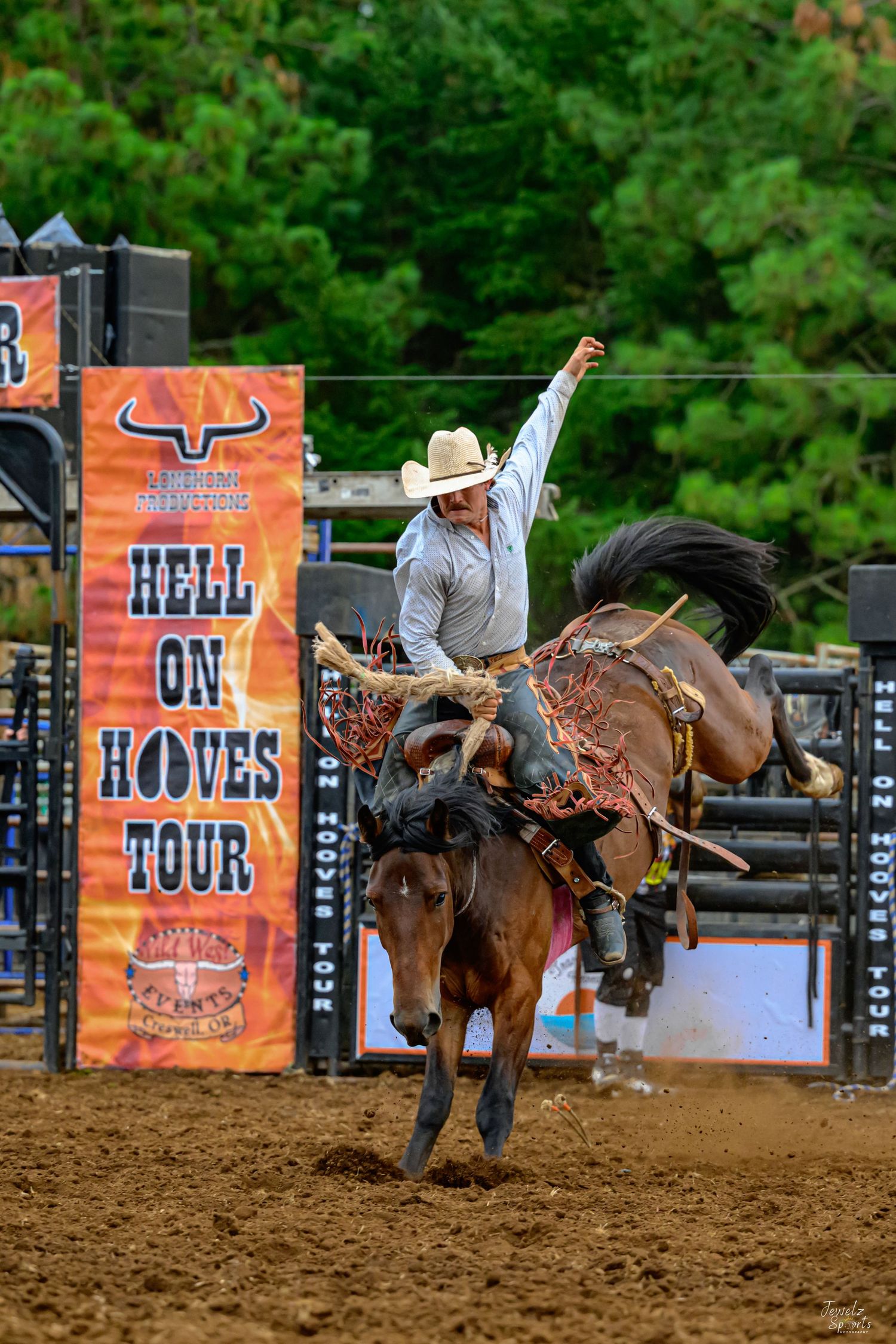 Cowboy riding bucking bronco at Hell on Hooves Tour rodeo event with one hand raised in the air.