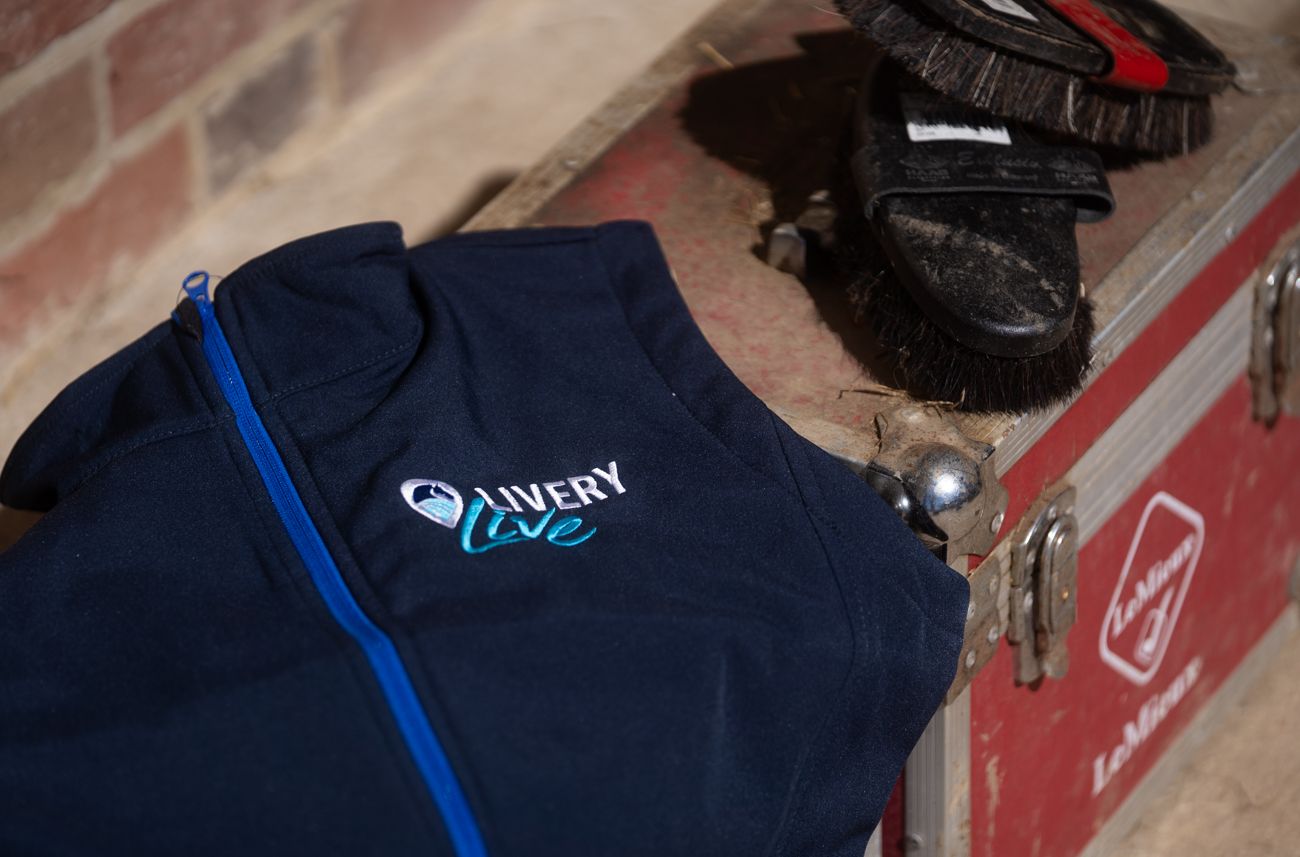 Navy blue Avery Live branded zip-up jacket with blue zipper, displayed next to shoes on a red case.