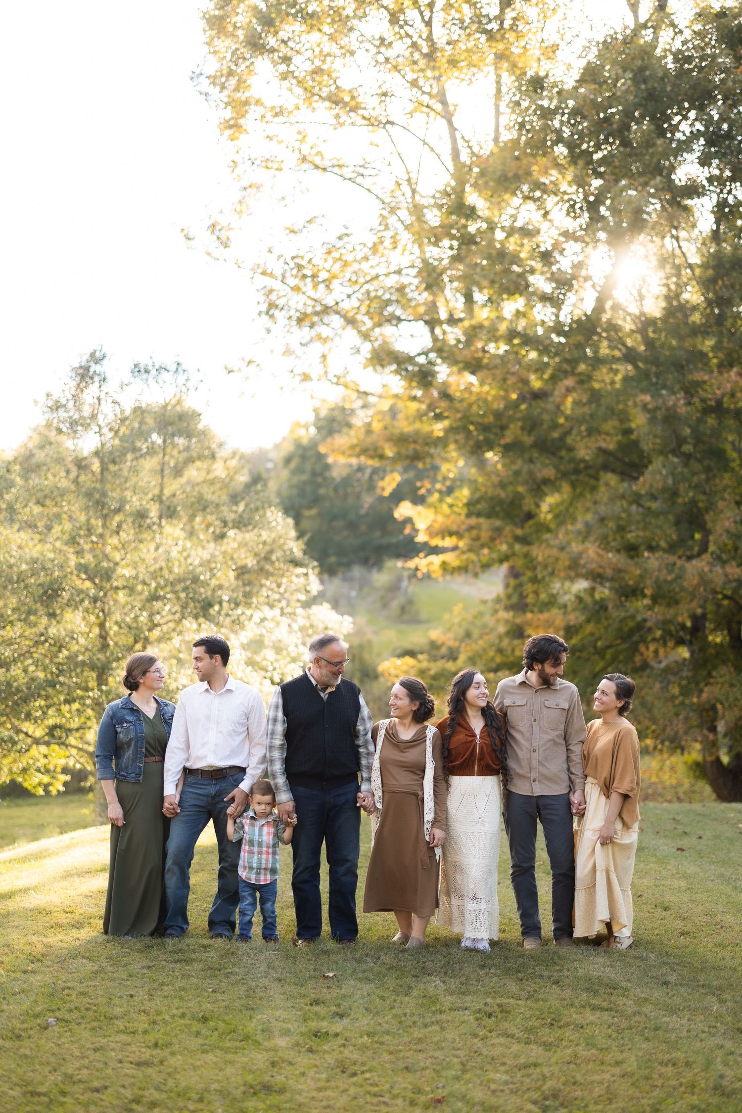 Multi-generational family group posing together outdoors in warm evening sunlight.