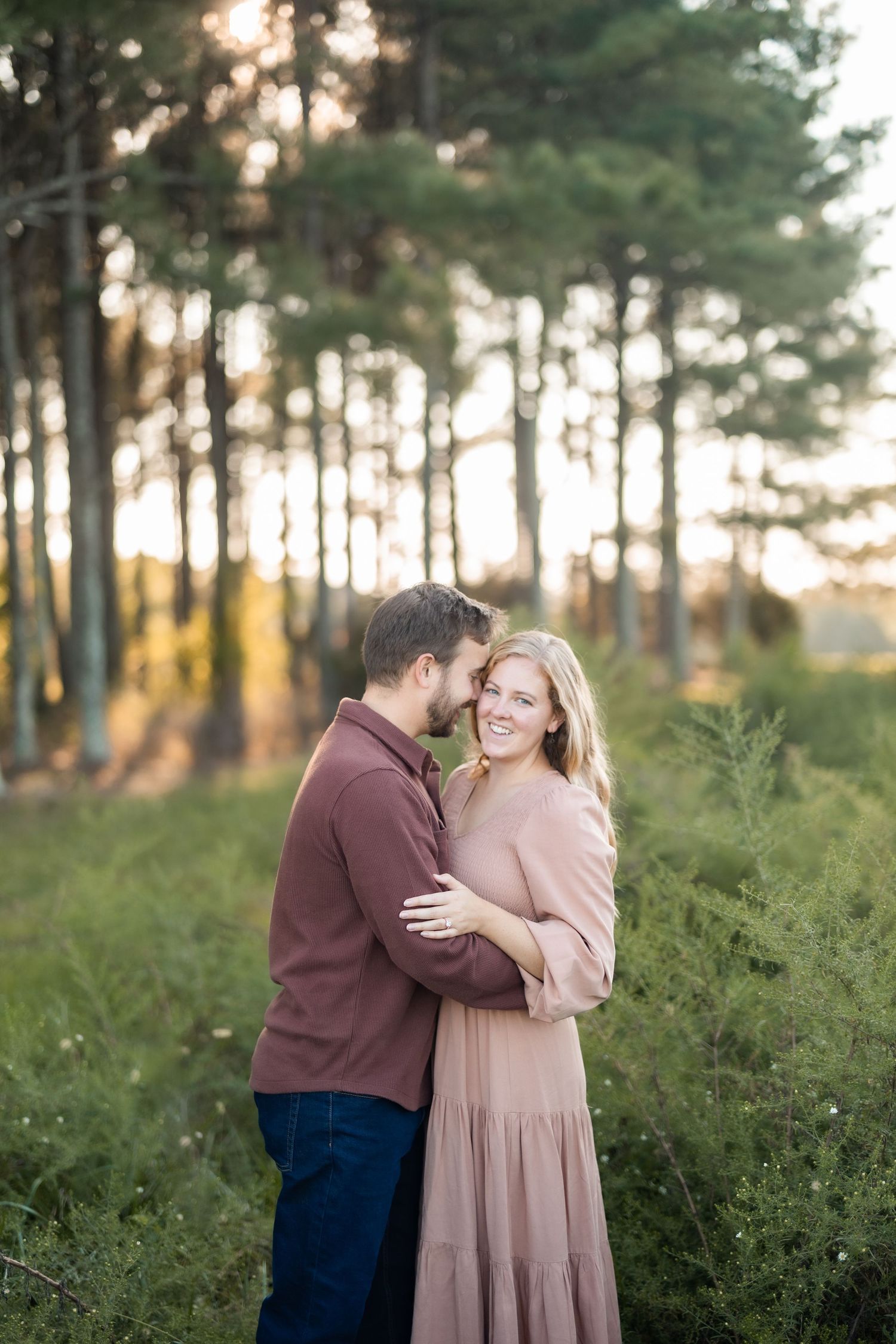 Couple embracing in a sunset-lit pine forest during engagement photos.