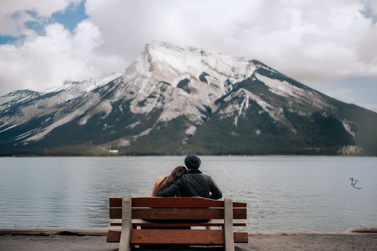 Indian couple sitting together on a bench, photo taken from behind with breathtaking Banff National Park mountain view